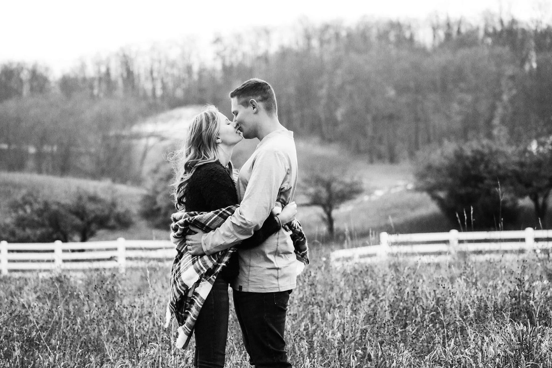 A black and white photo of a man and woman kissing in a field.