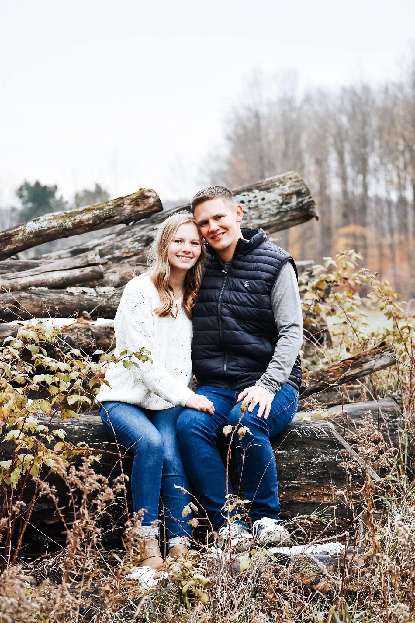 A man and a woman are sitting on a pile of logs.