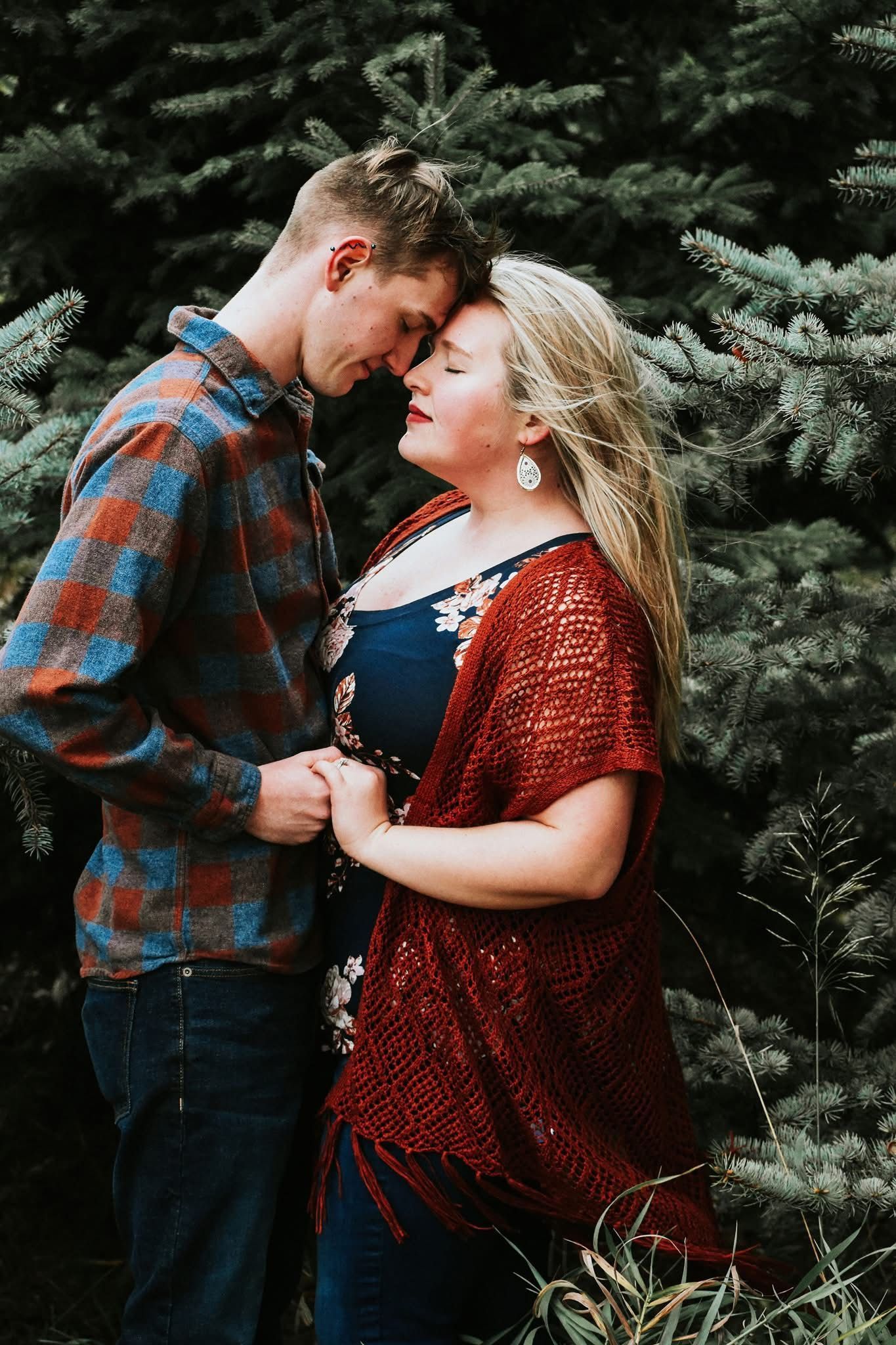 A man and a woman are standing next to each other in the woods holding hands.