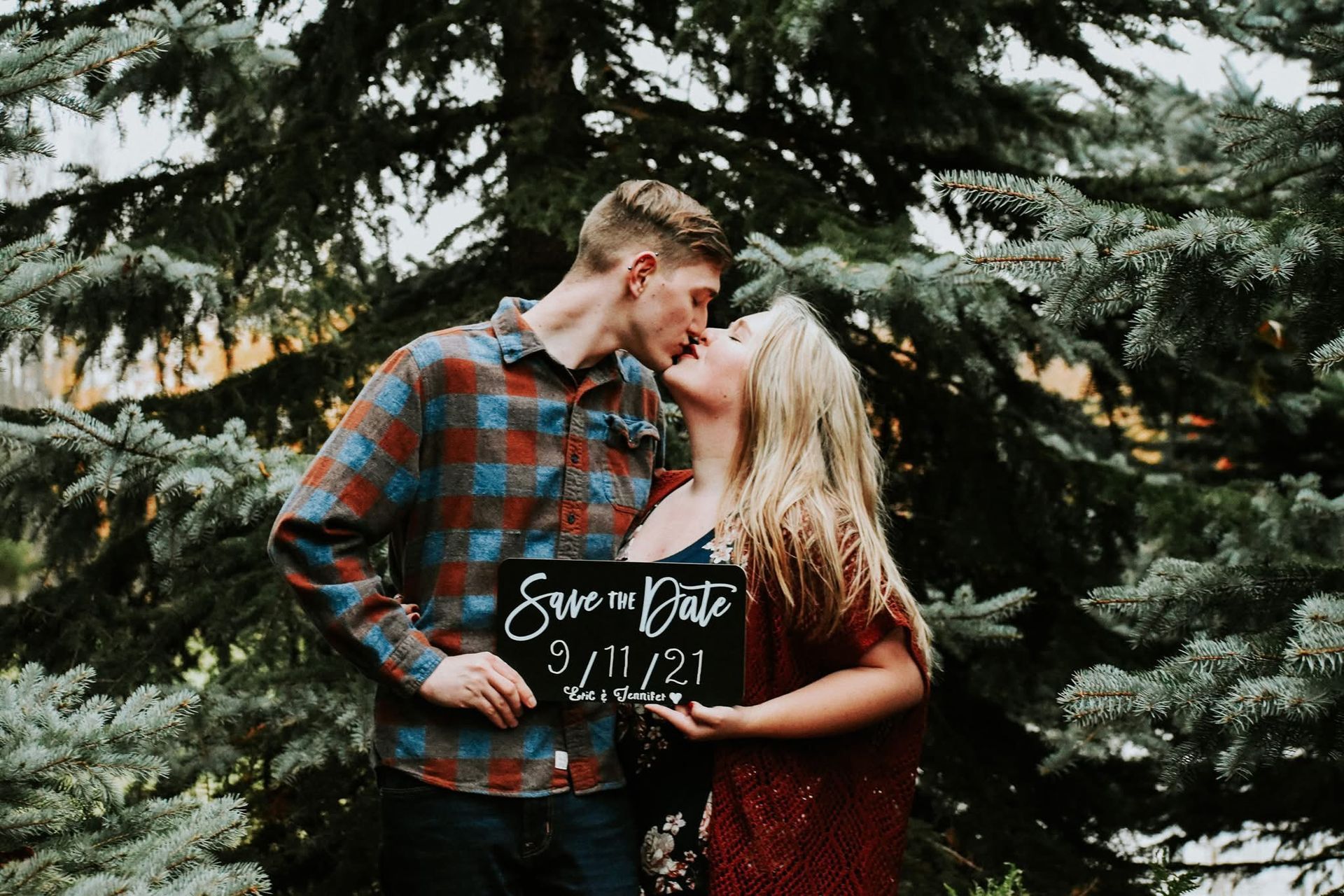 A man and a woman are kissing while holding a sign that says save the date.