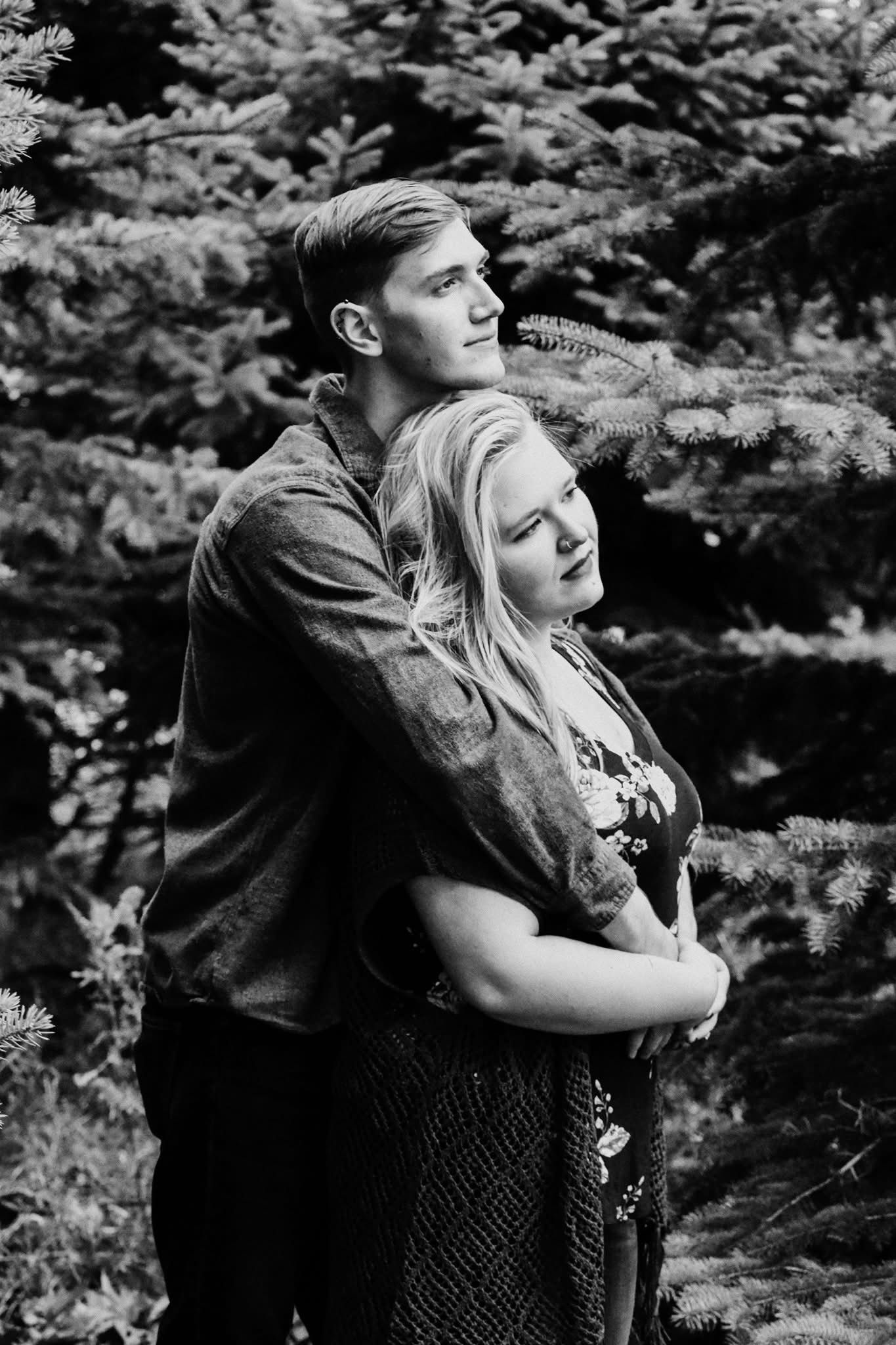 A black and white photo of a man and woman hugging in the woods.