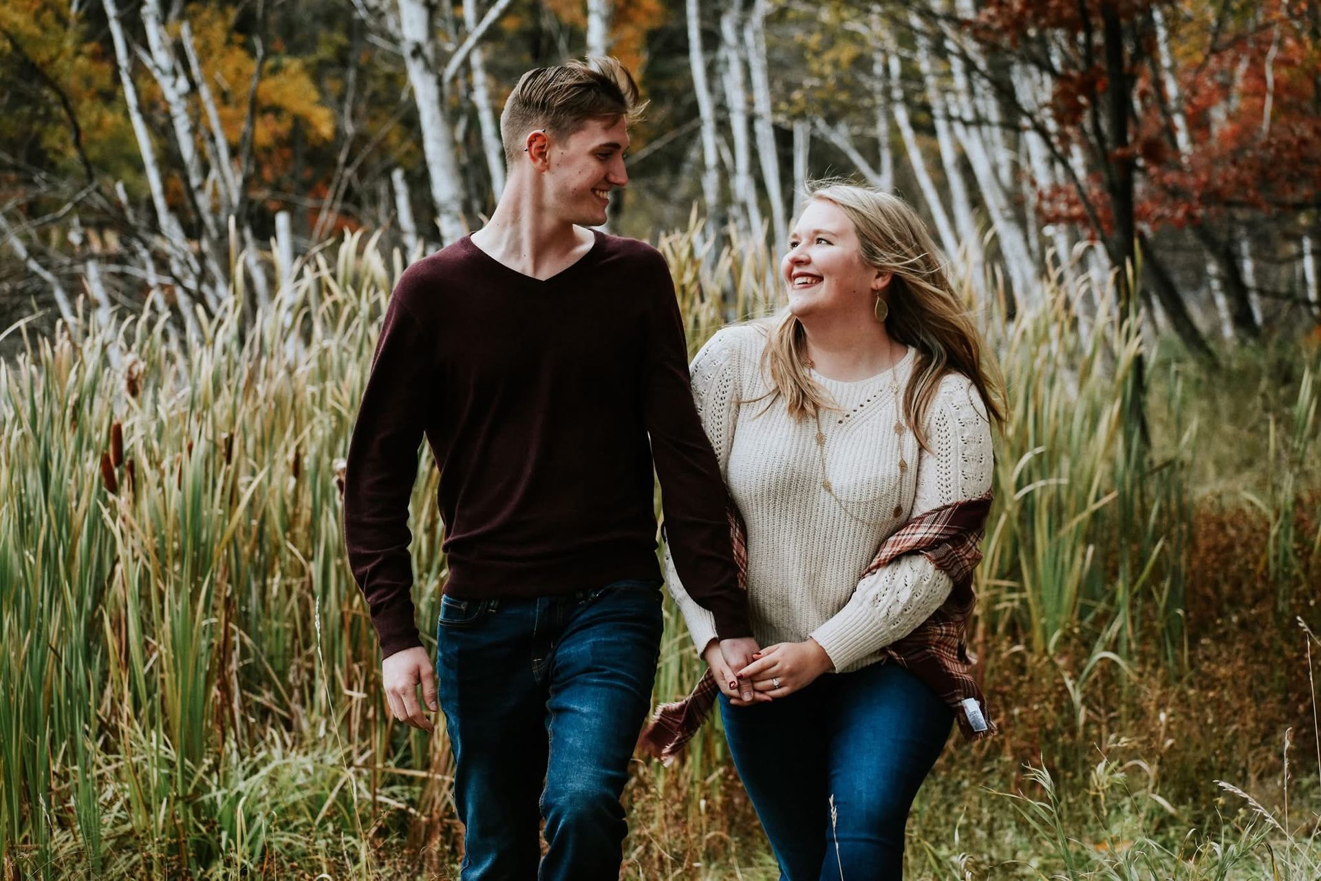 A man and a woman are holding hands while walking through a field.