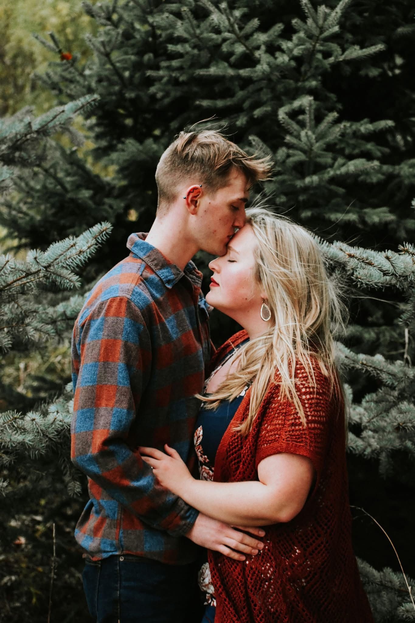 A man and a woman are kissing in front of a christmas tree.