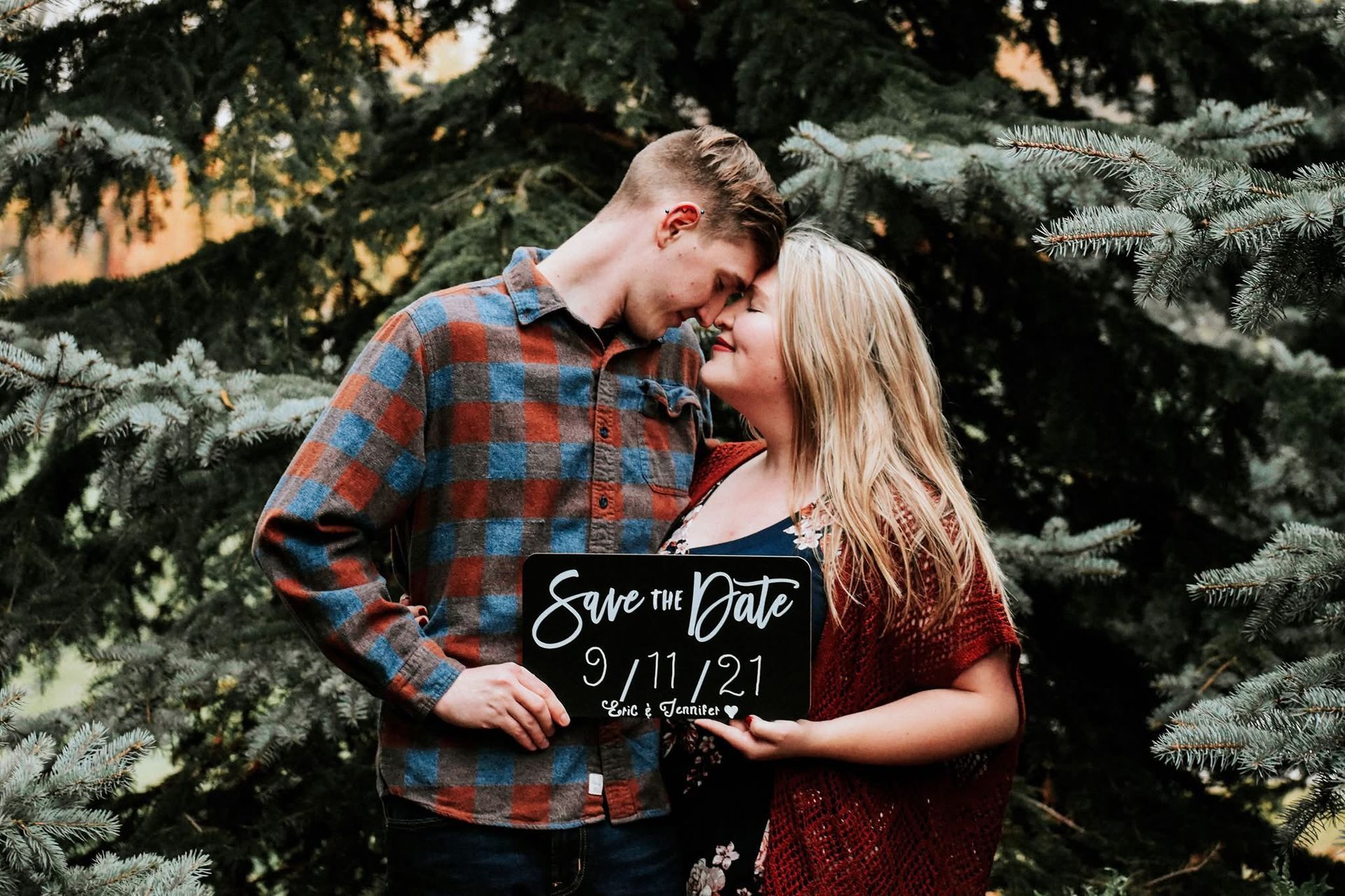 A man and a woman are standing next to each other holding a save the date sign.