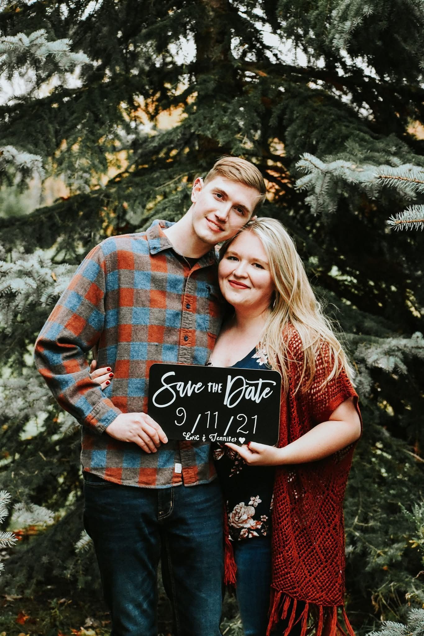 A man and a woman are standing next to each other holding a sign that says save the date.