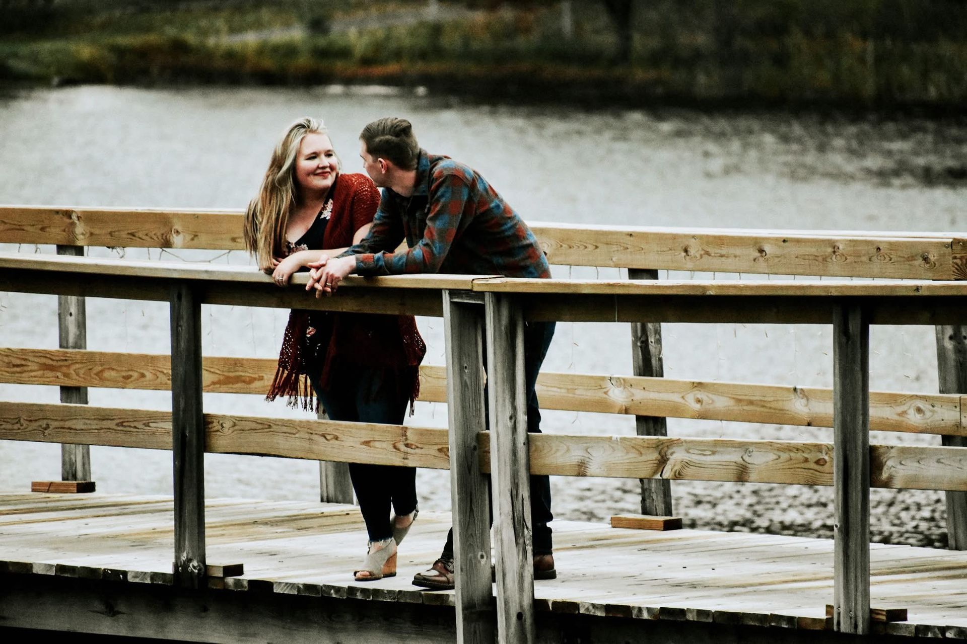 A man and a woman are standing on a wooden bridge over a lake.