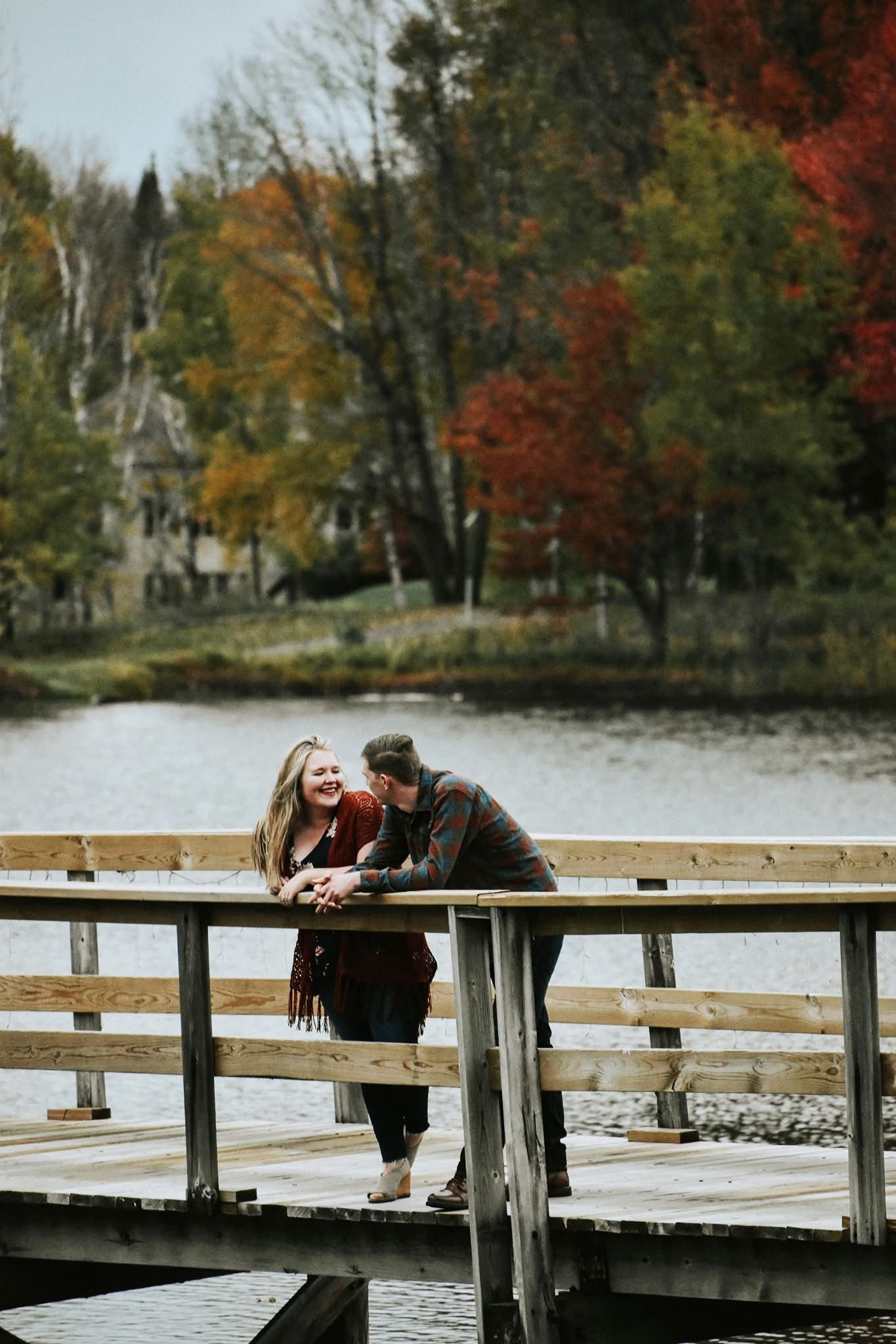 A man and a woman are standing on a wooden bridge over a body of water.