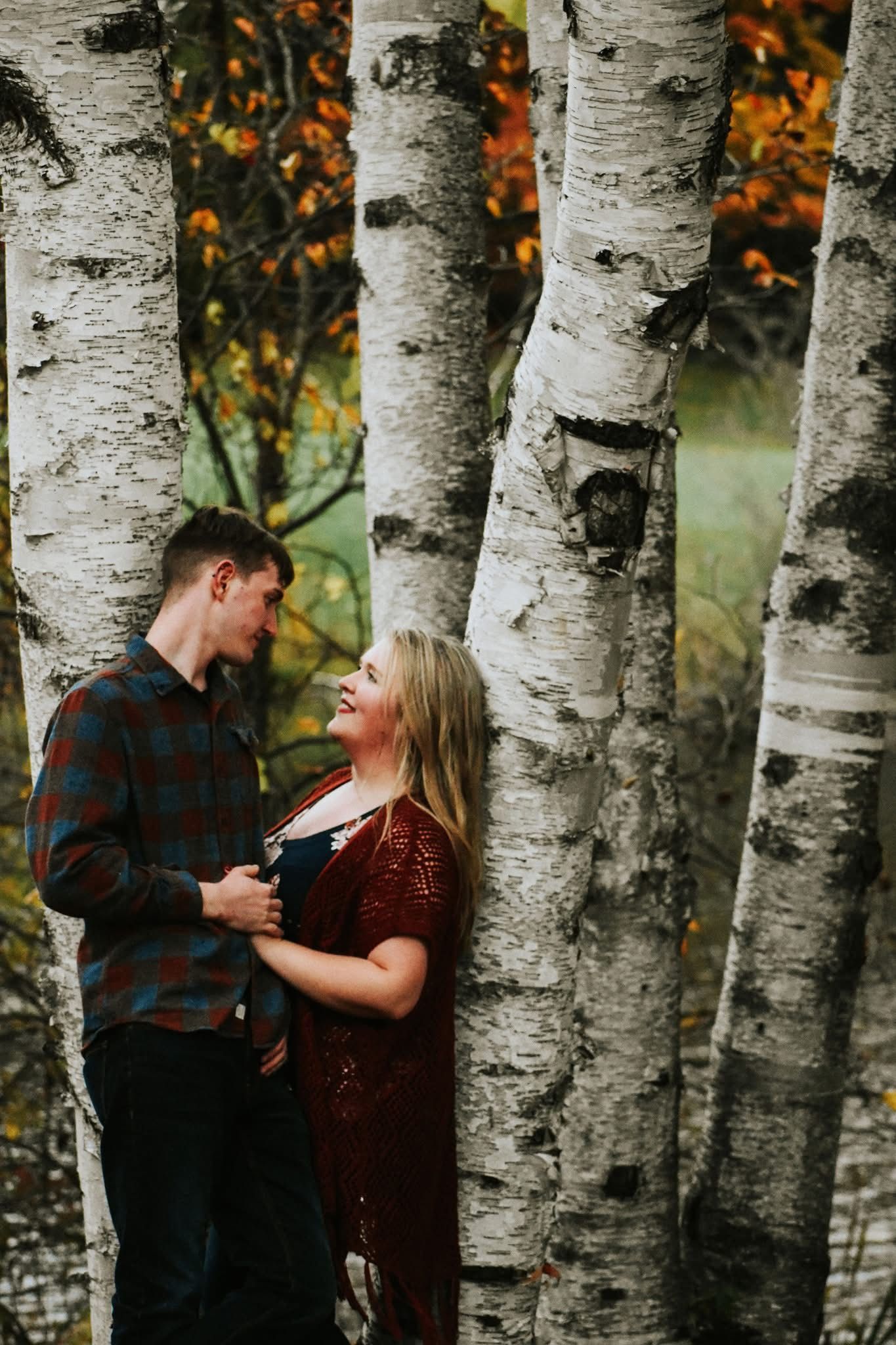 A man and a woman are leaning against a tree in a forest.