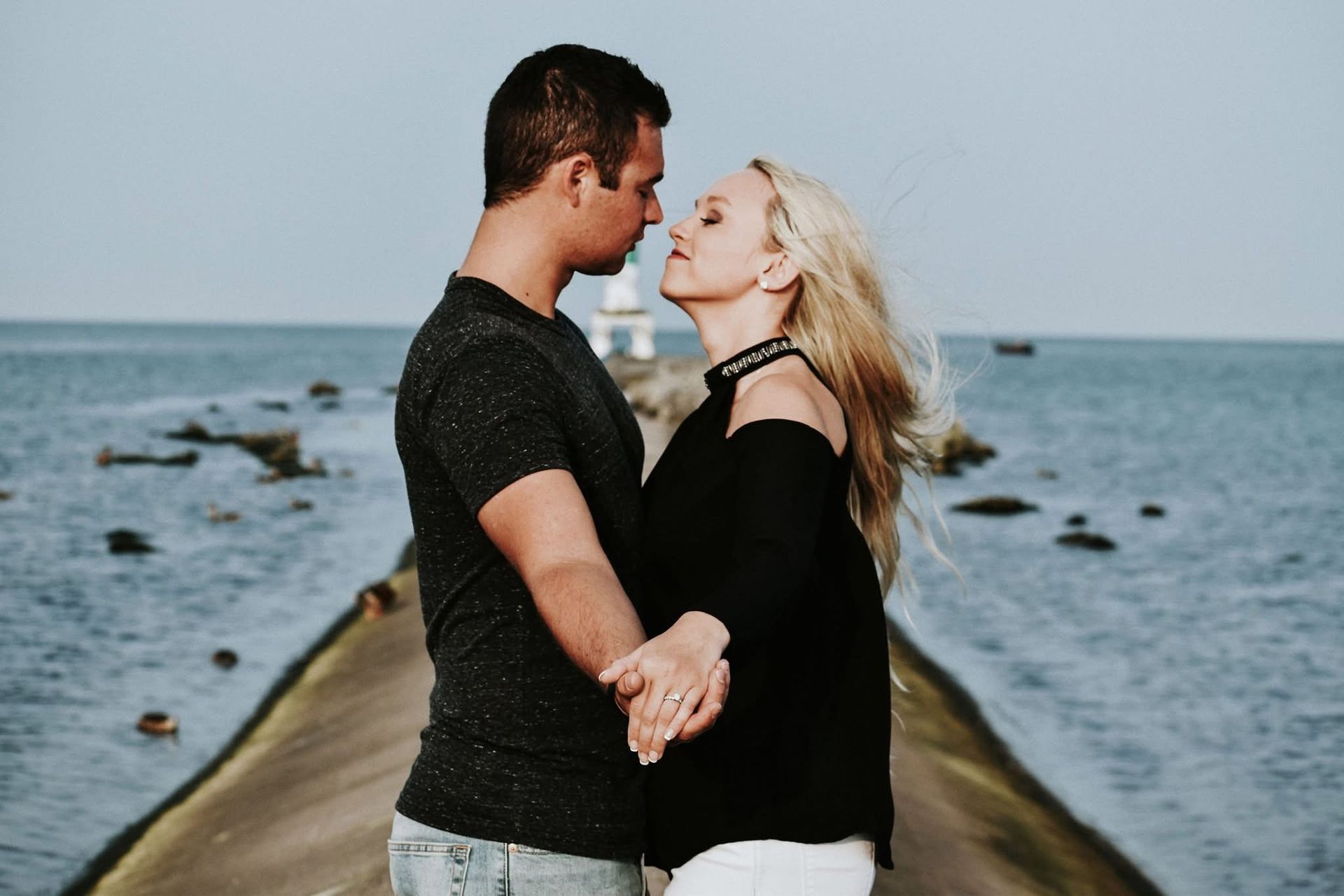 A man and a woman are standing on a pier holding hands and looking at each other.