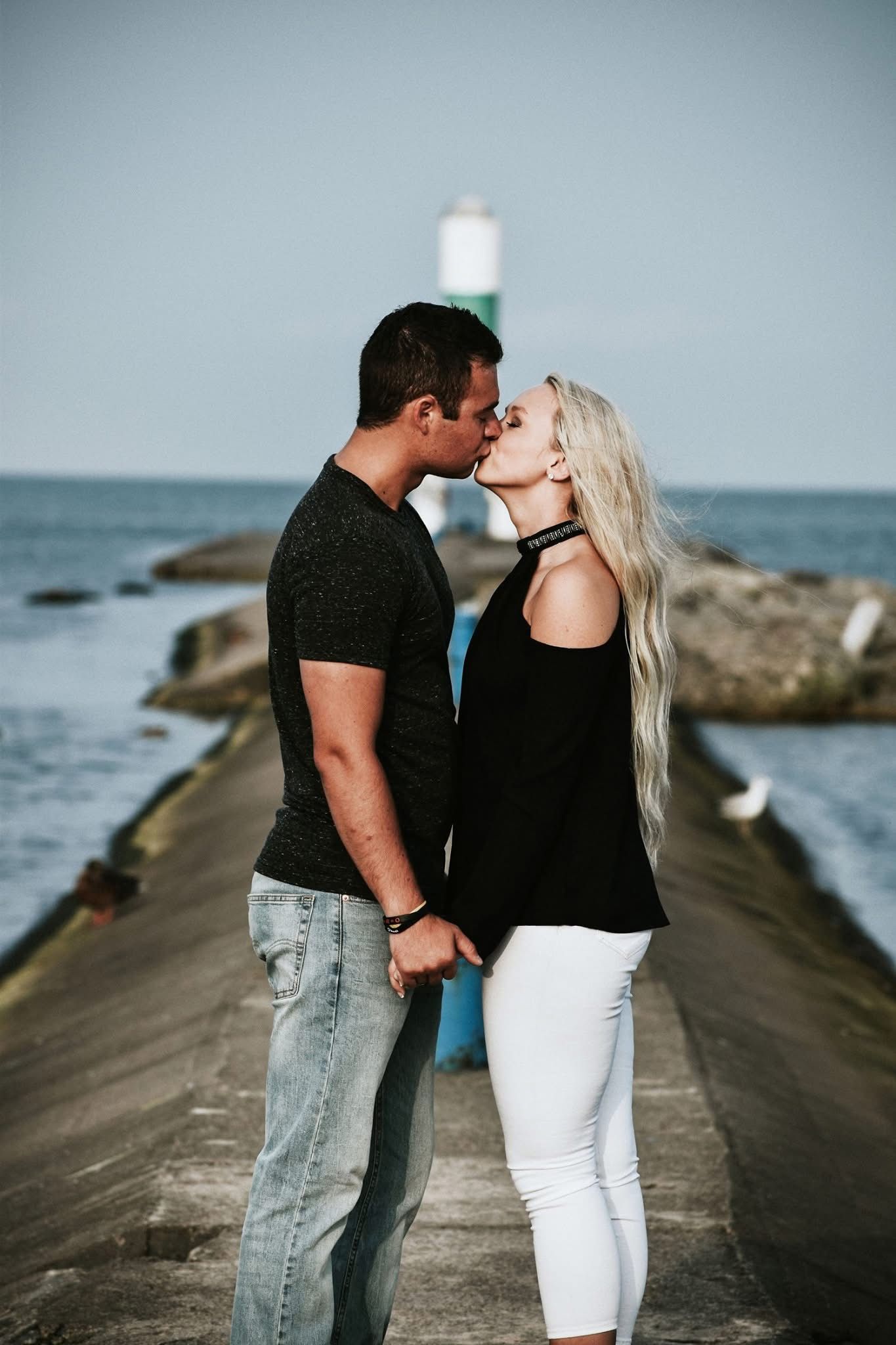 A man and a woman are kissing on a pier.