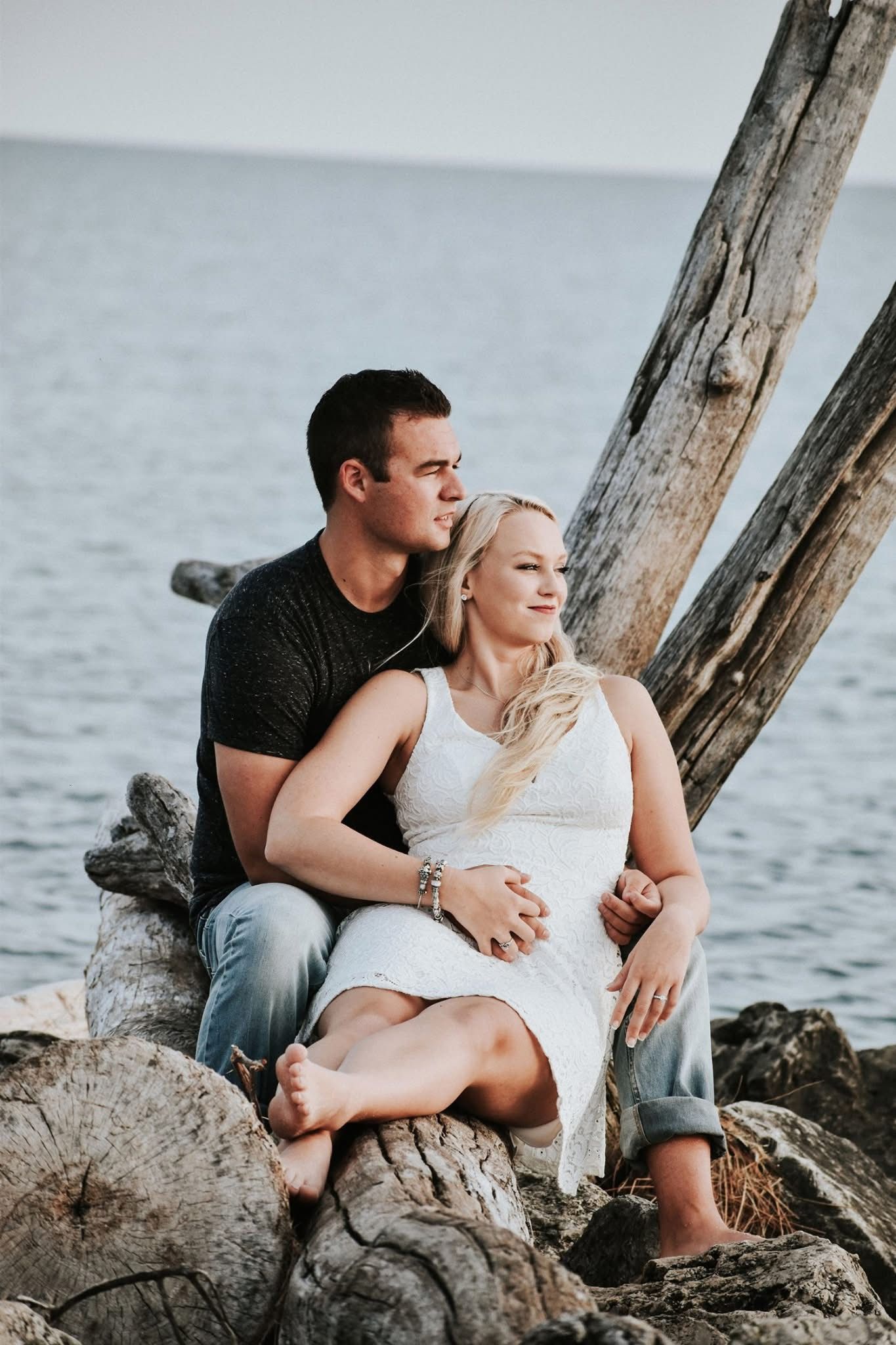 A man and a woman are sitting on a rock near the water.