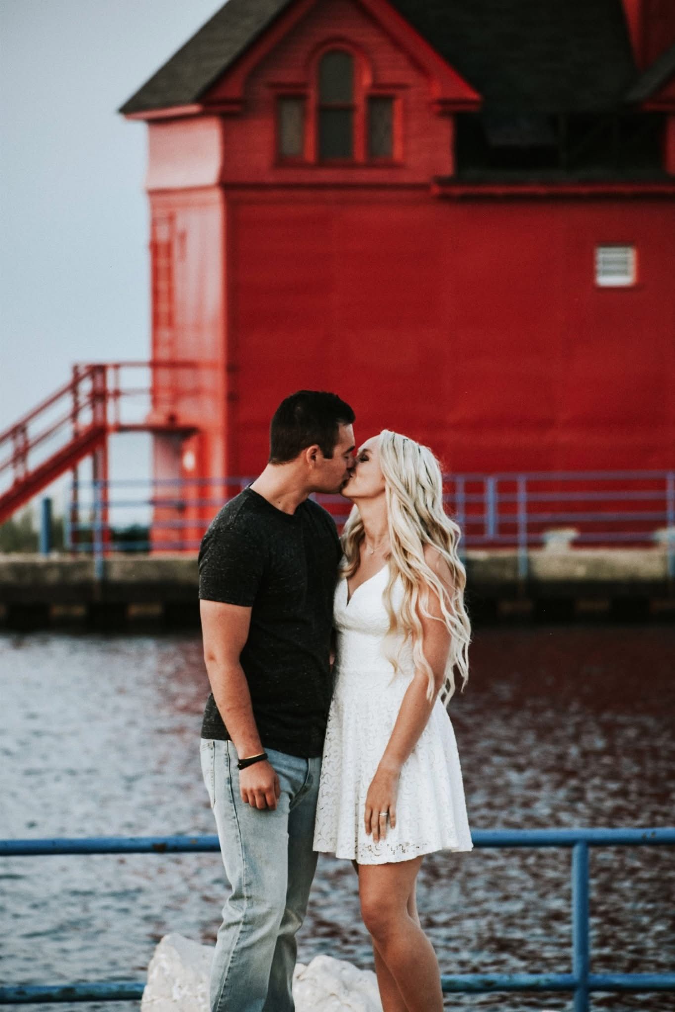 A man and a woman are kissing in front of a red lighthouse.