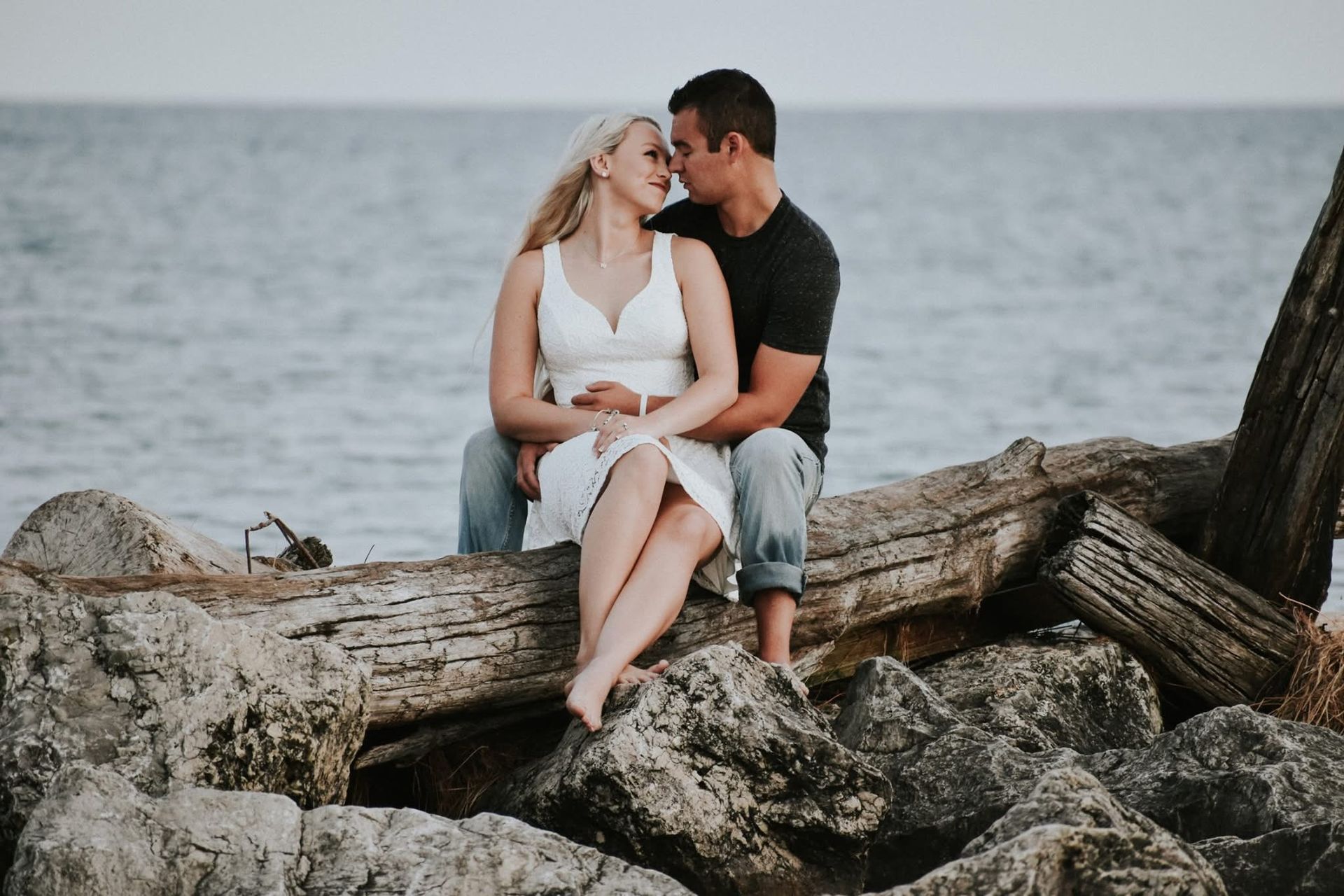A man and a woman are sitting on a log near the ocean.