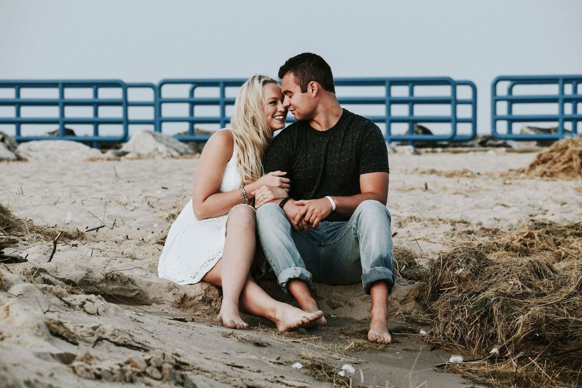 A man and a woman are sitting on the beach looking at each other.
