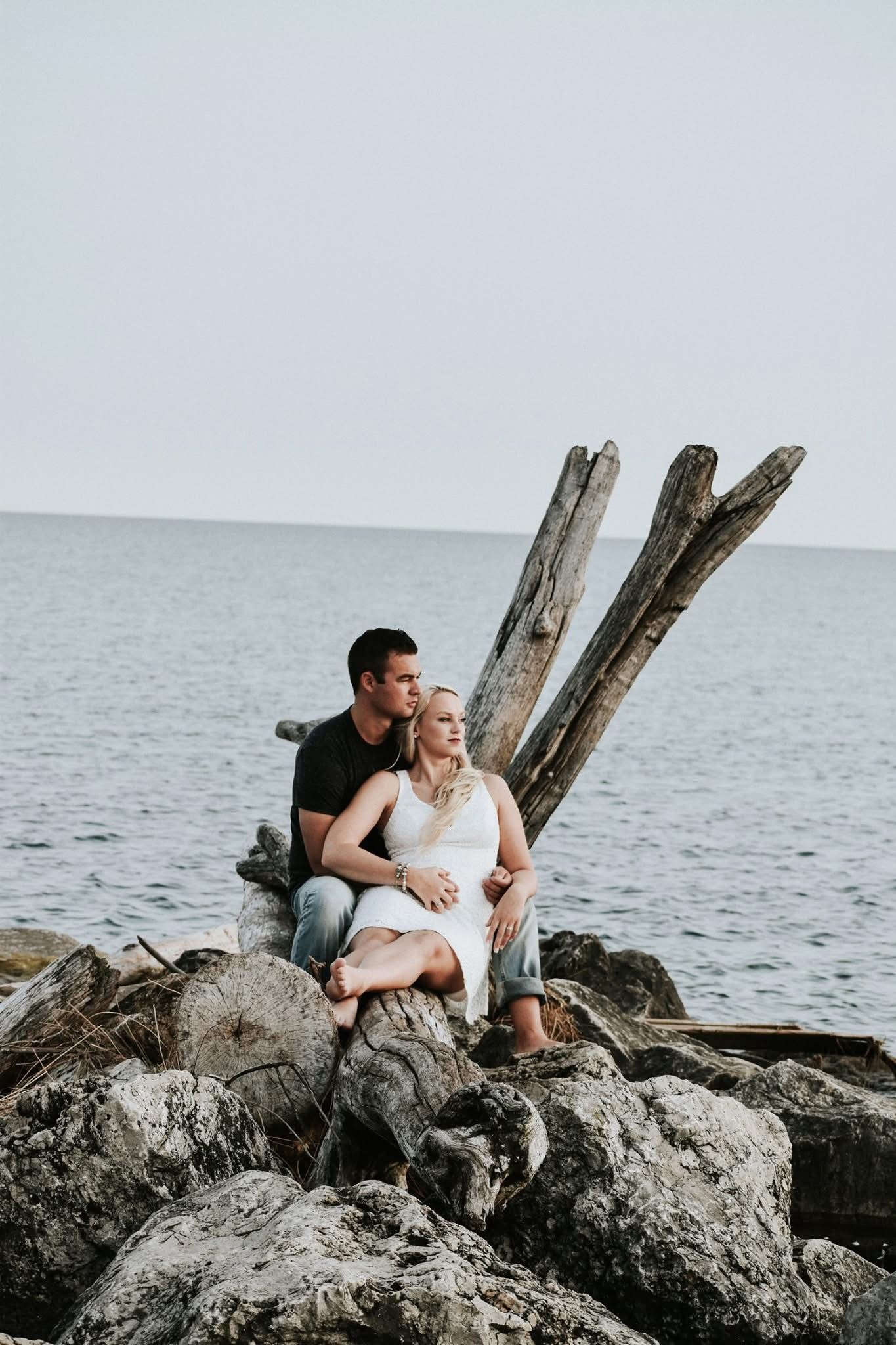A man and a woman are sitting on rocks near the ocean.