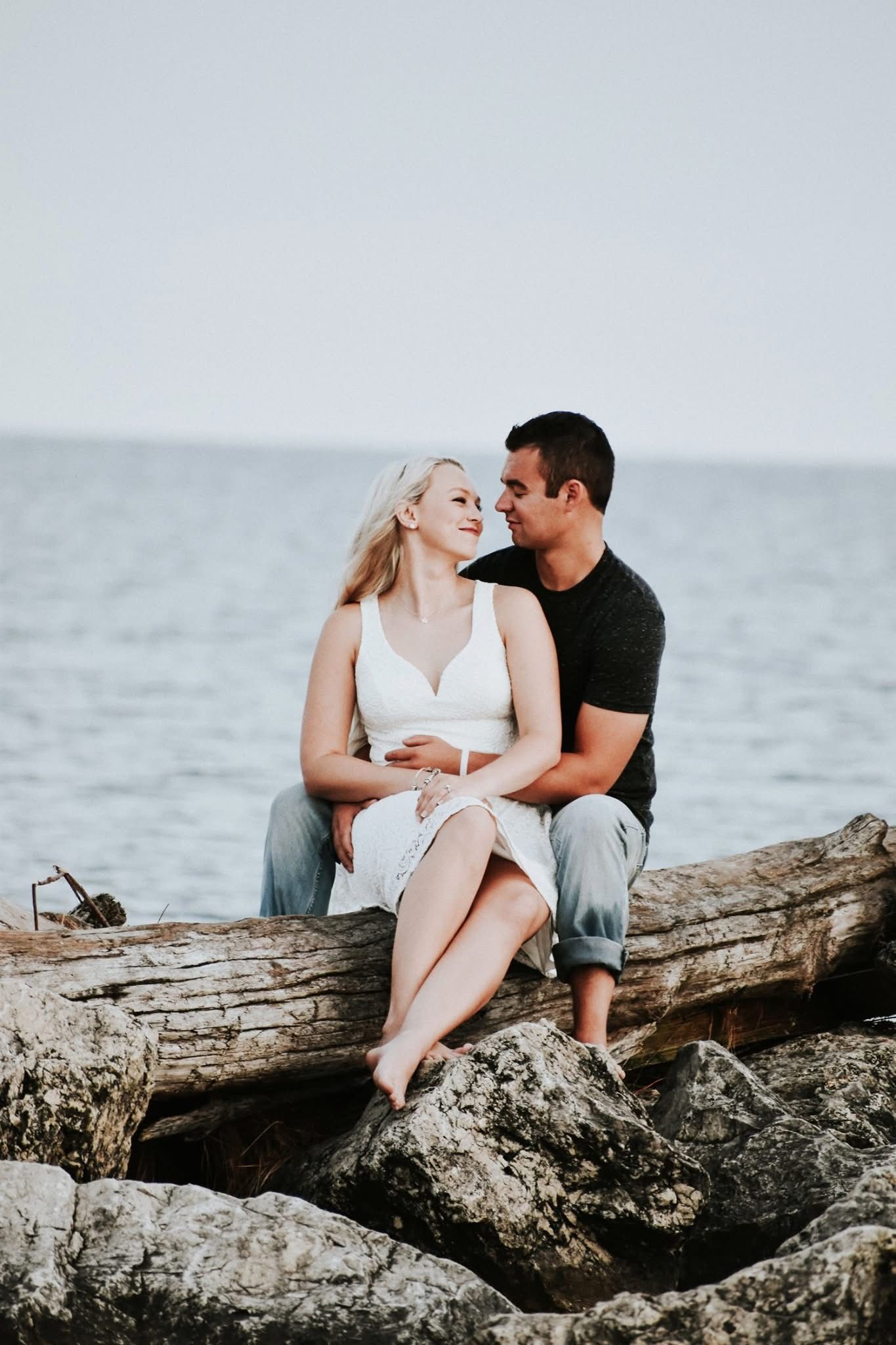 A man and a woman are sitting on a log near the ocean.