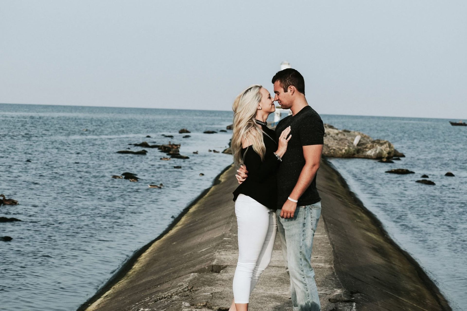 A man and a woman are kissing on a pier overlooking the ocean.