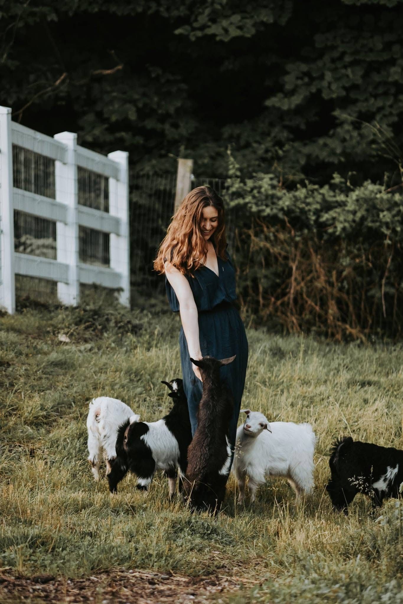 A woman is standing next to a herd of goats in a field.