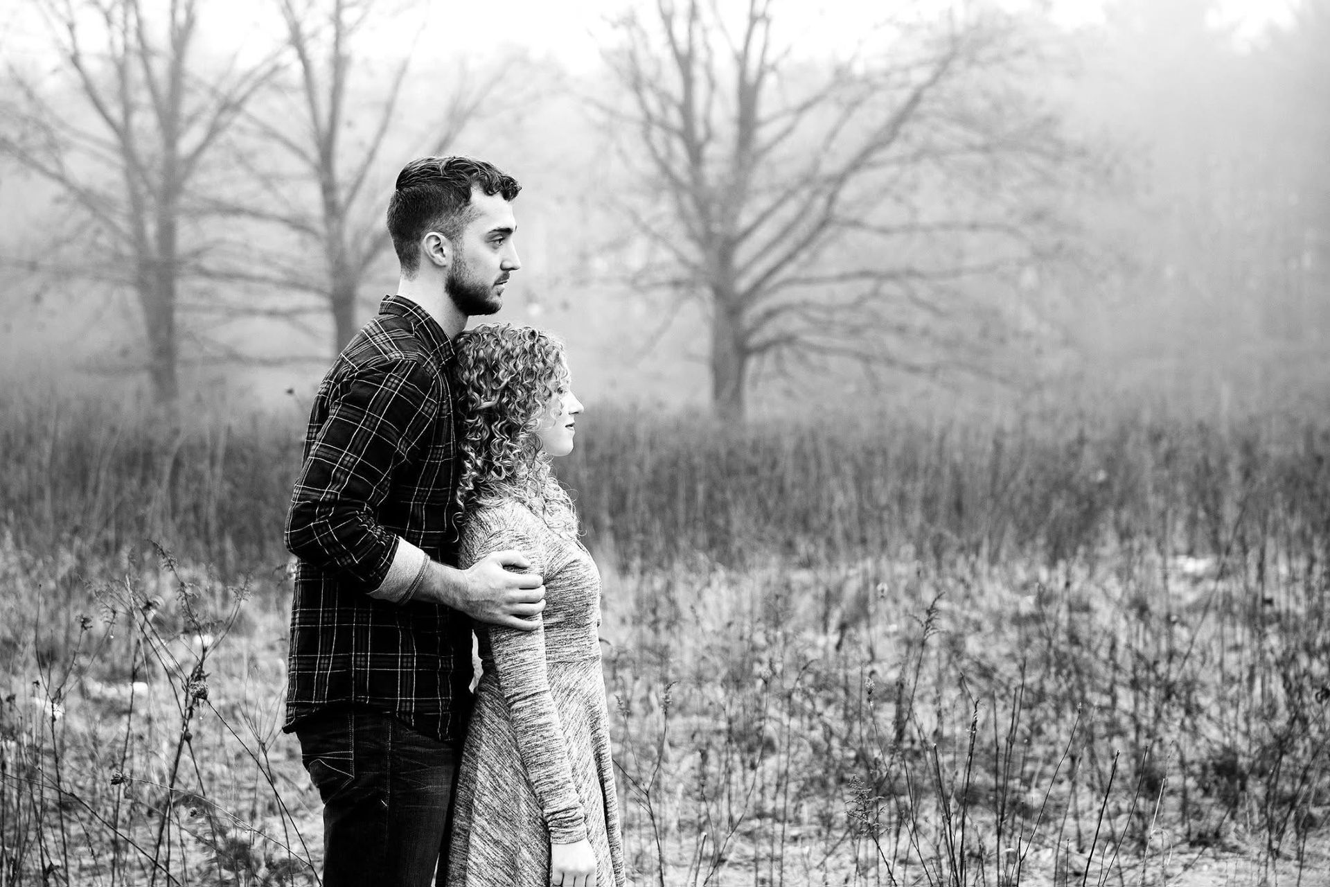 A black and white photo of a man and woman hugging in a field.