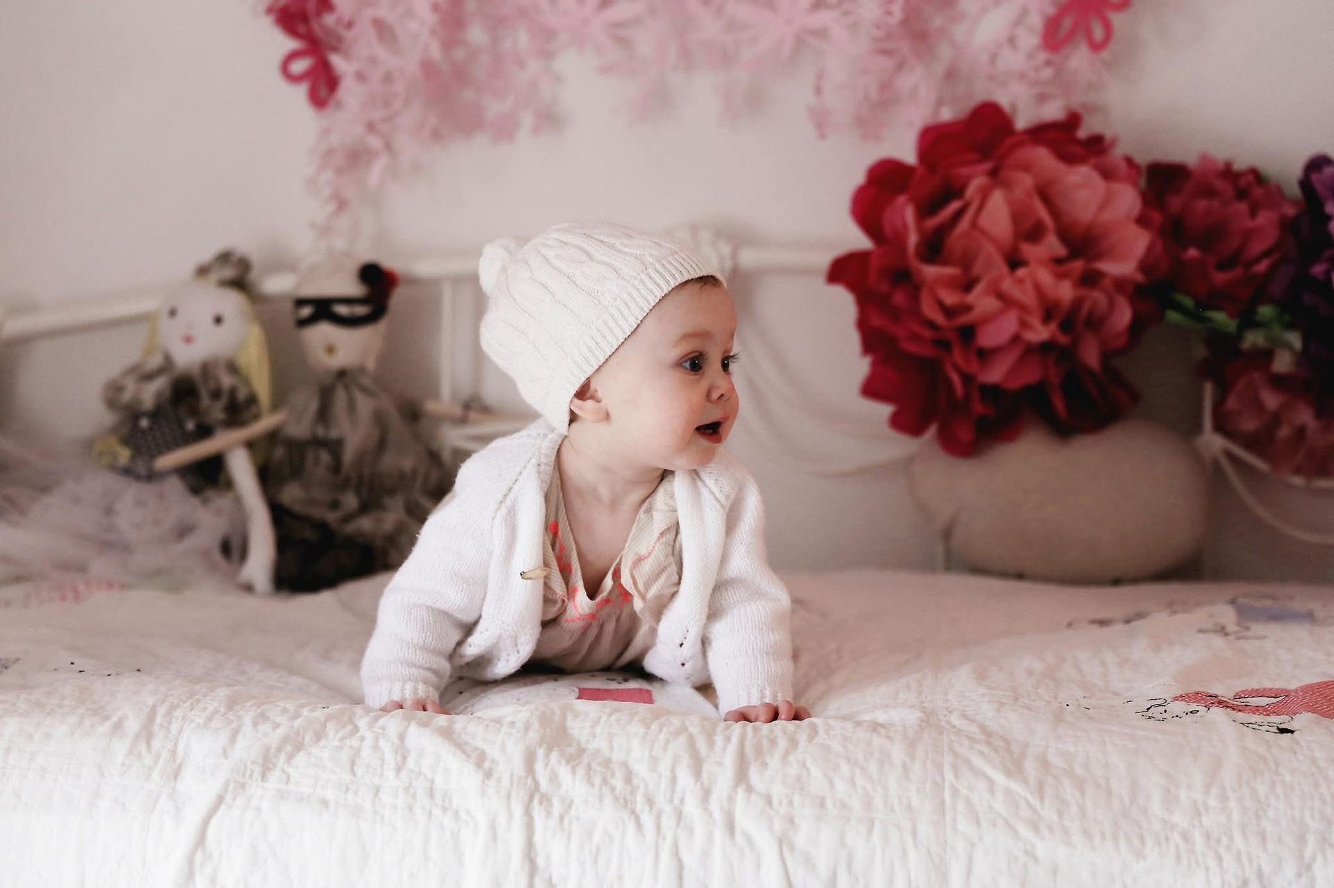 A baby is crawling on a bed wearing a white hat.