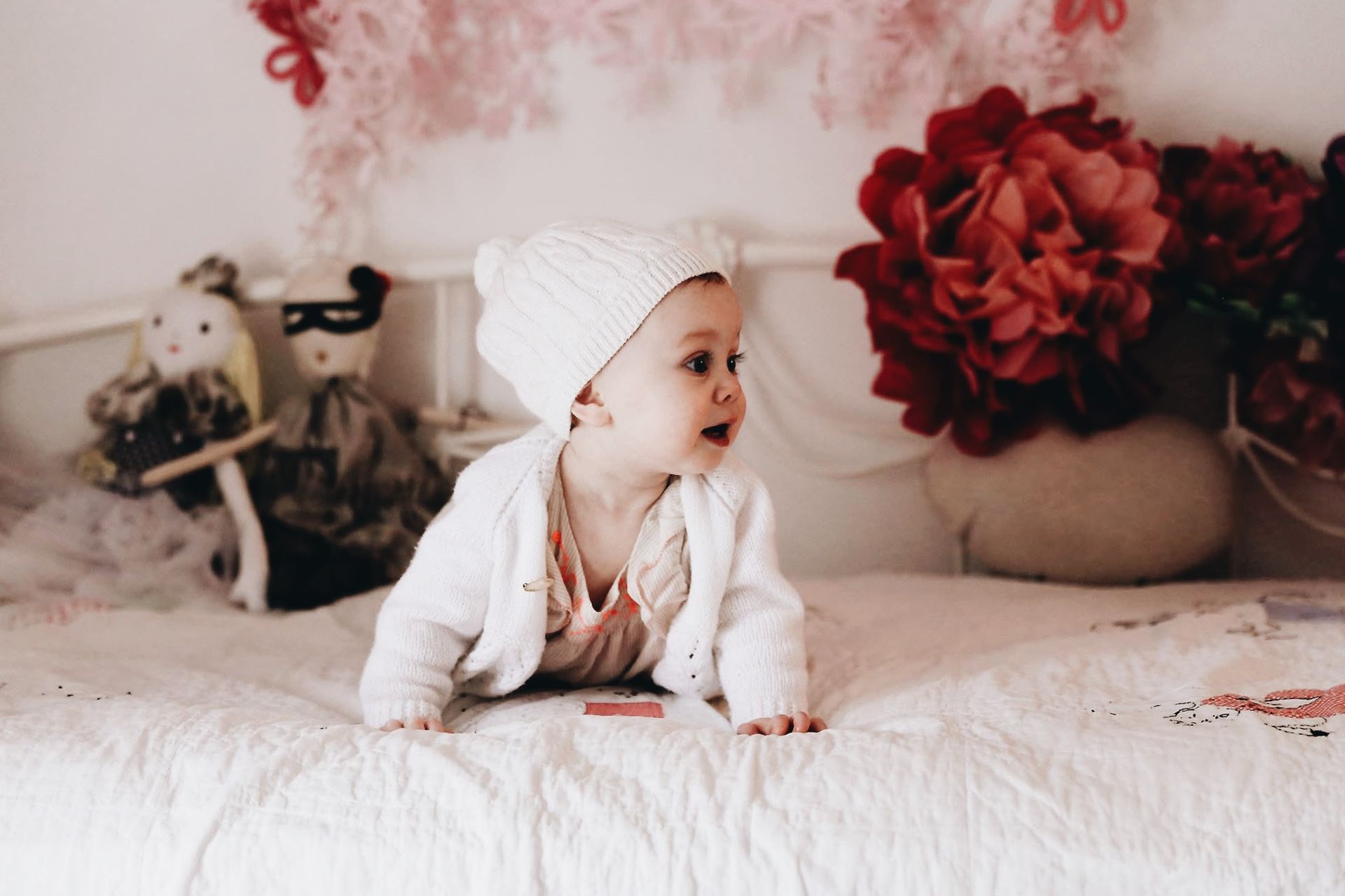 A baby is crawling on a bed wearing a white hat.