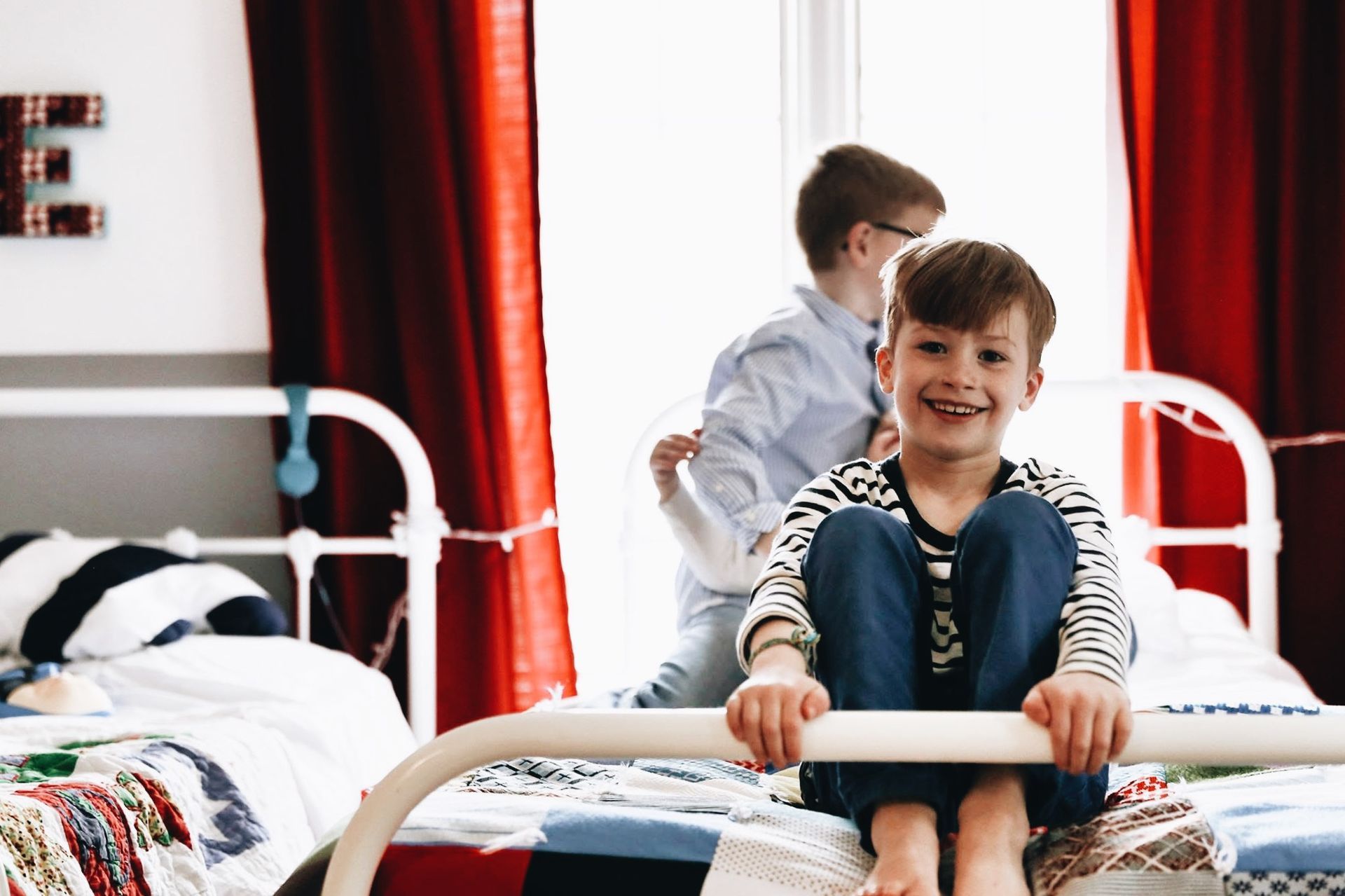 Two young boys are playing on a bed in a bedroom.