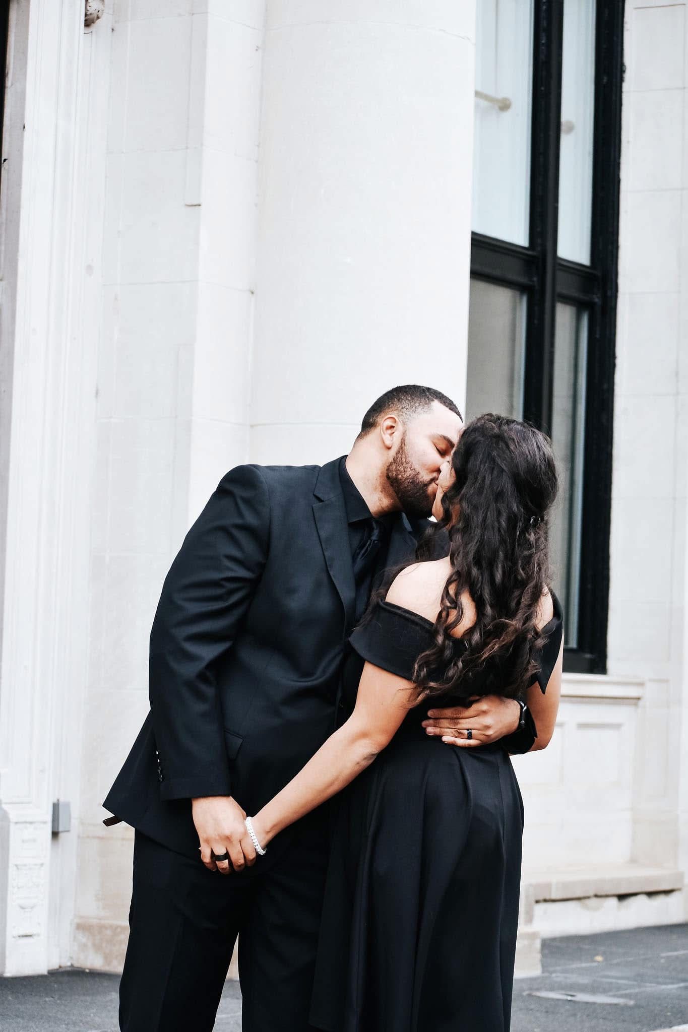 A man in a suit kissing a woman in a black dress