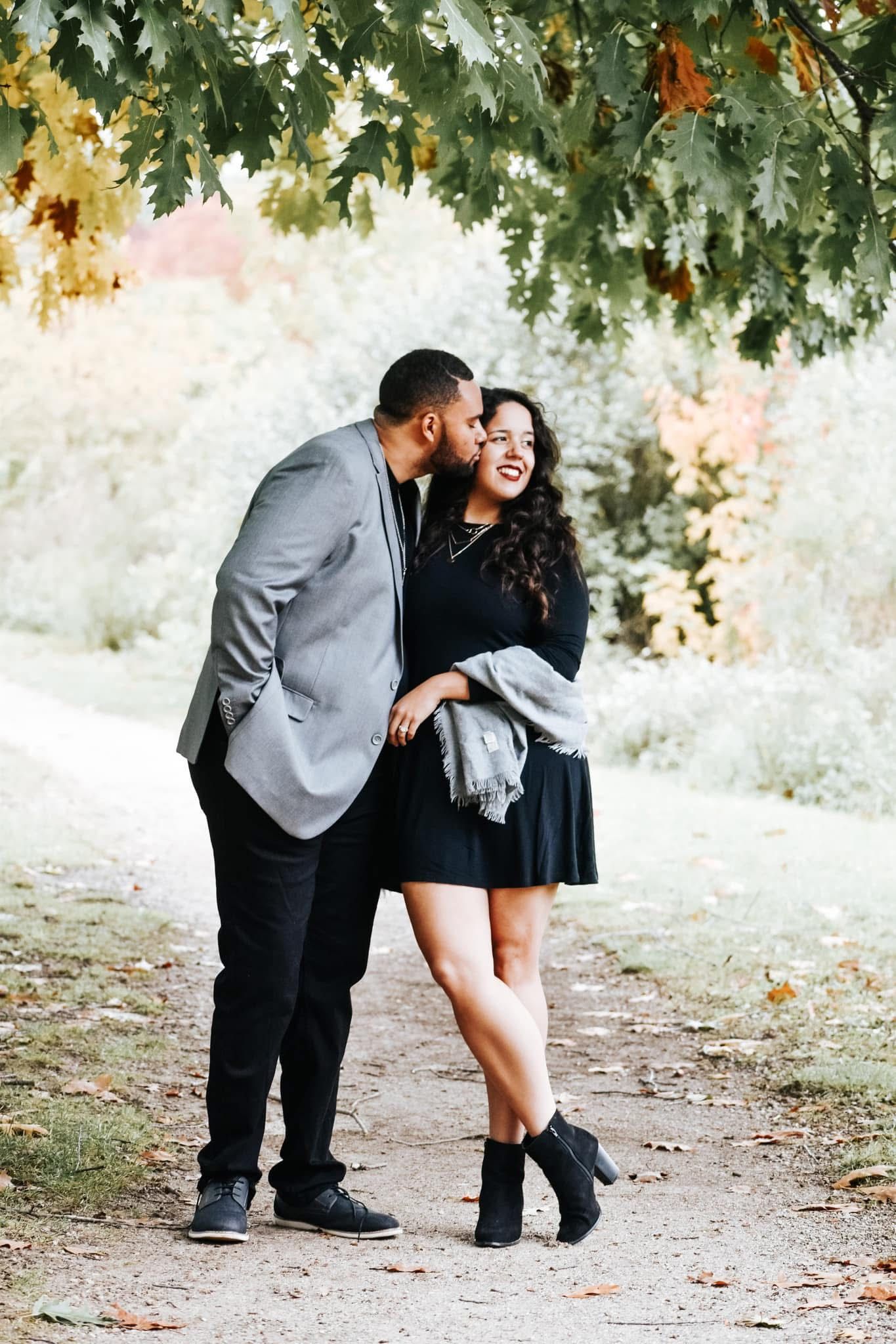 A man is kissing a woman on the cheek in a park.