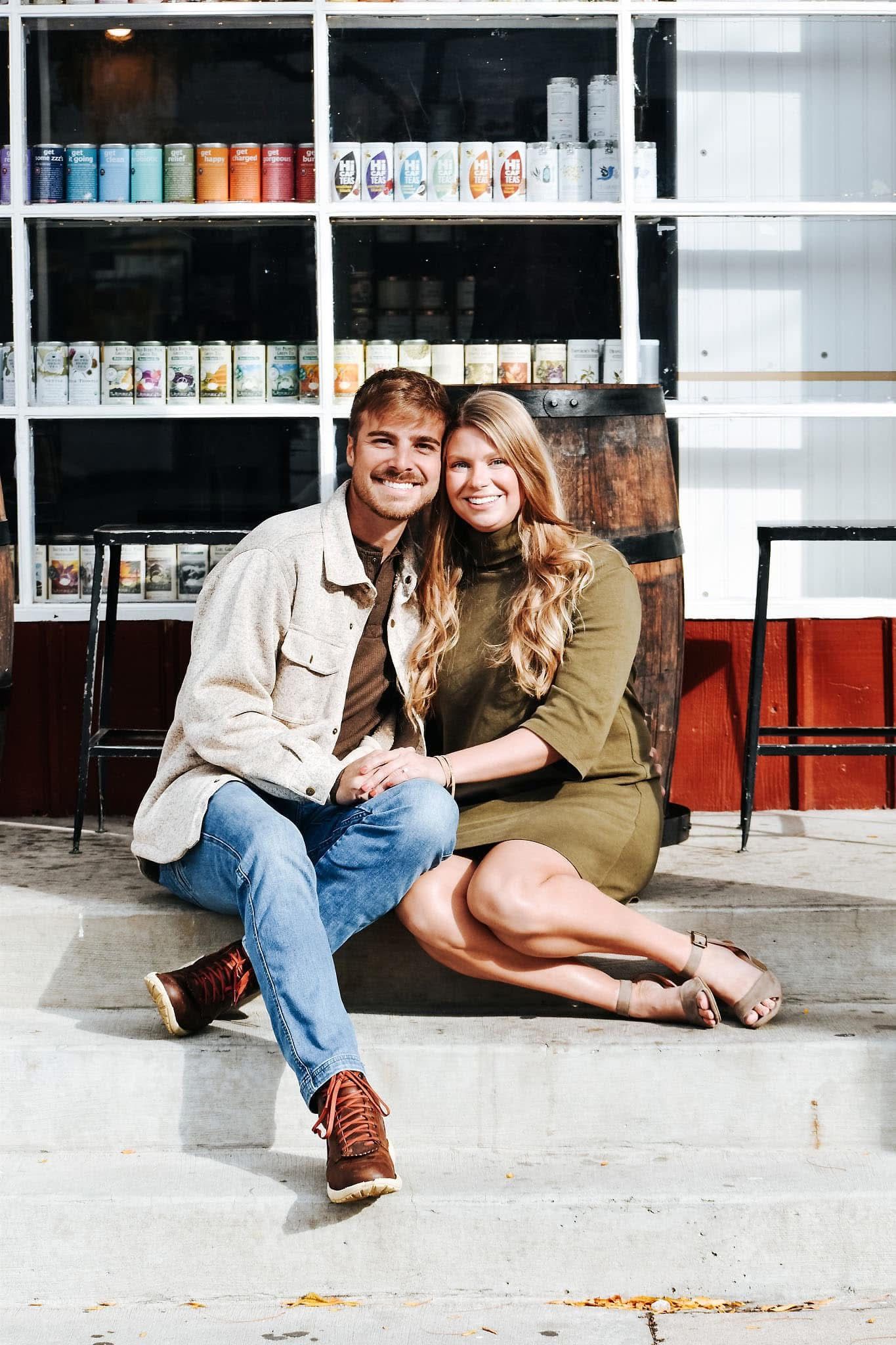 A man and a woman are sitting on the sidewalk in front of a store.
