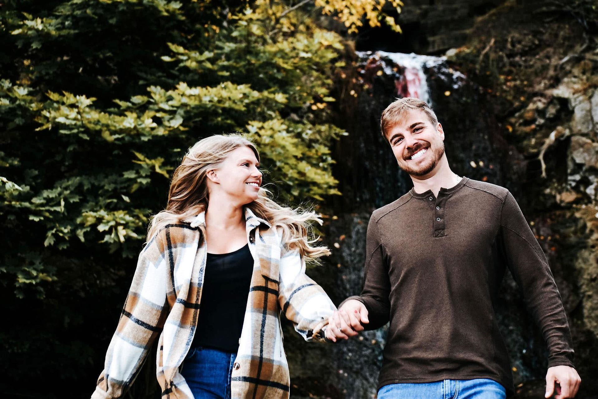 A man and a woman are holding hands in front of a waterfall.