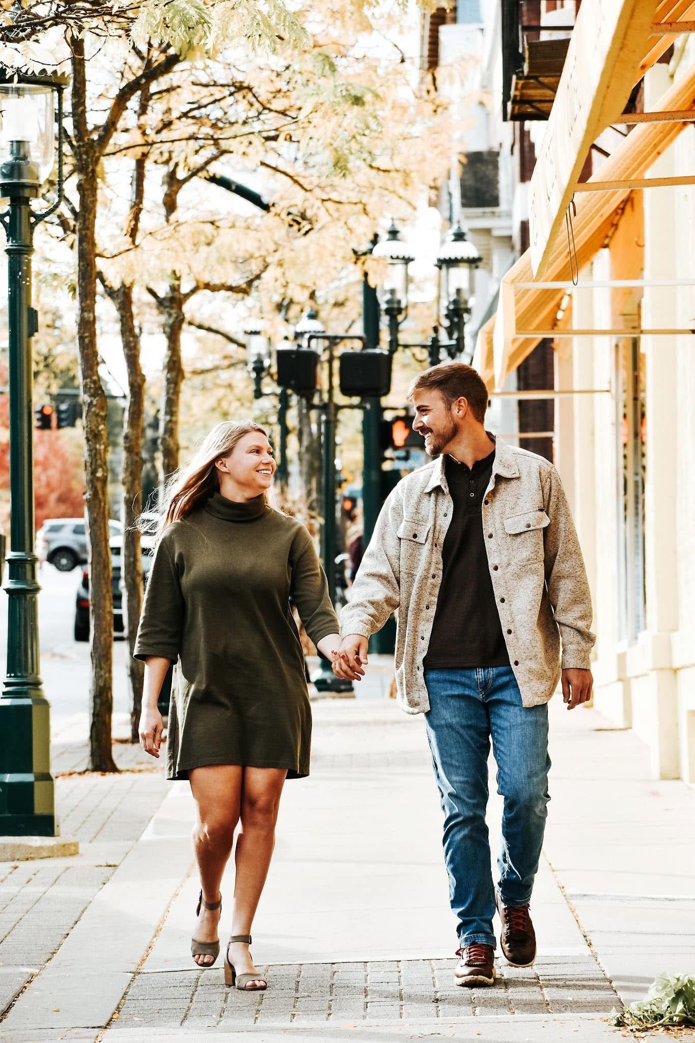 A man and a woman are walking down a sidewalk holding hands.