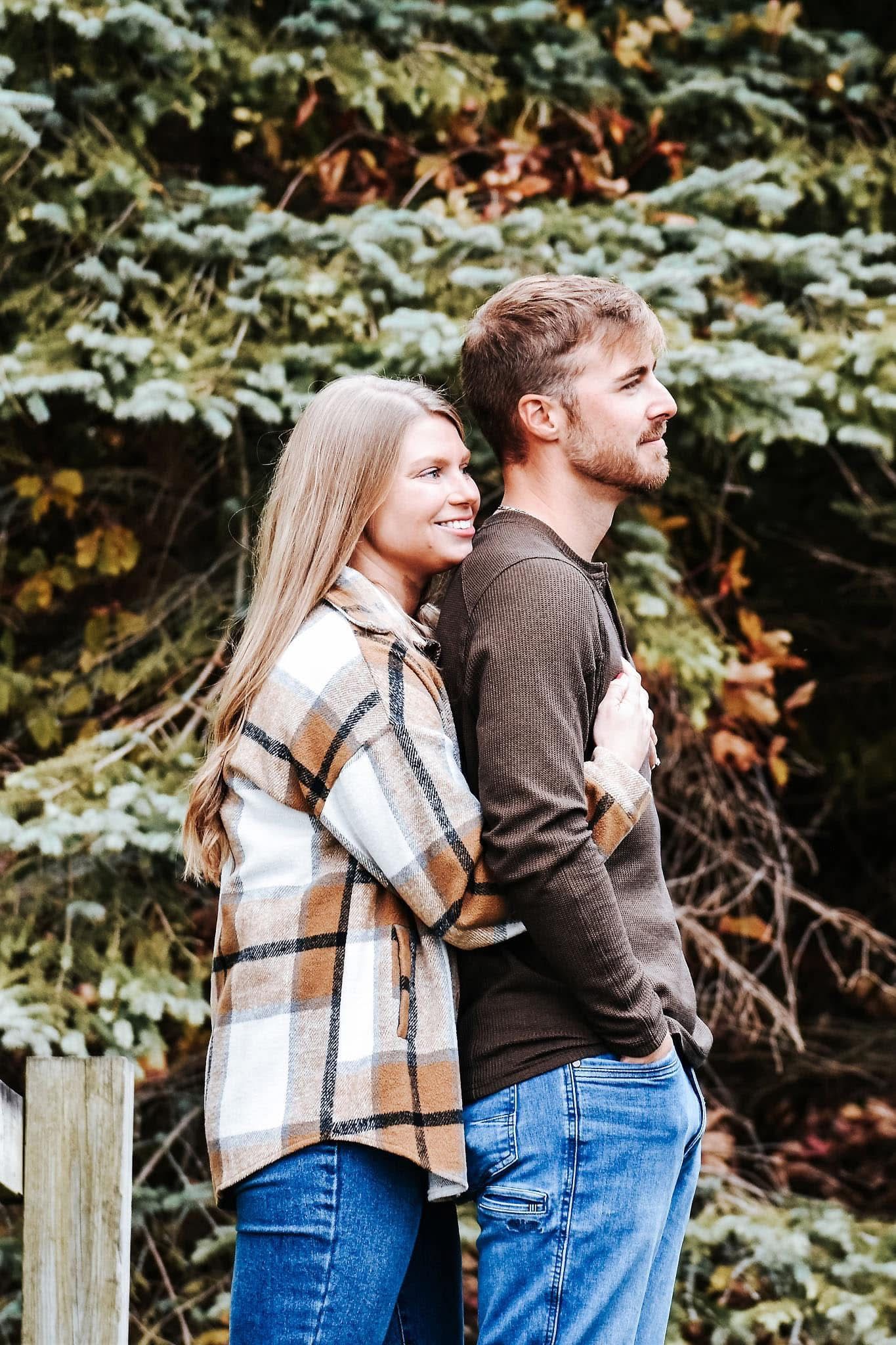 A man and a woman are standing next to each other in front of trees.
