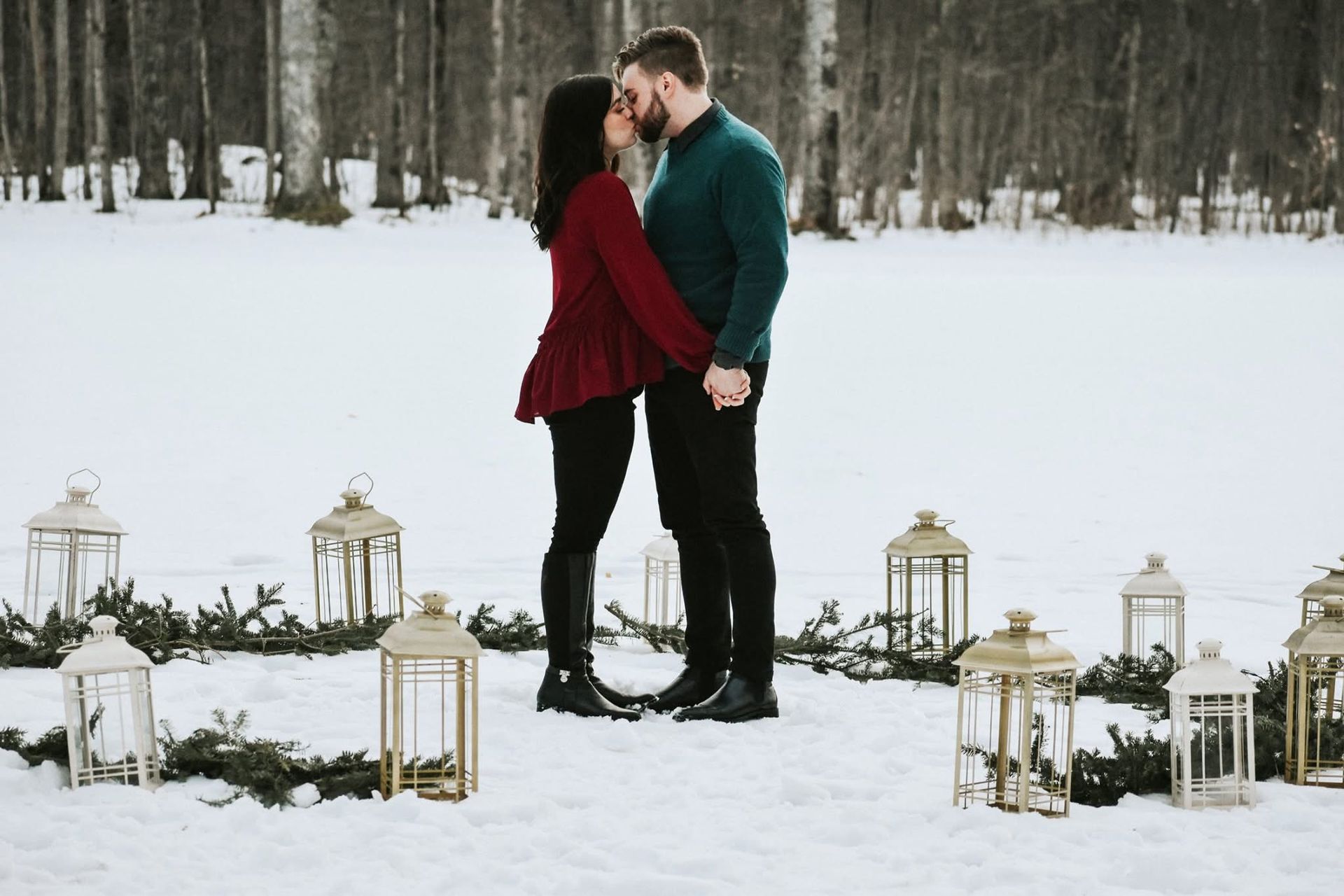 A man and a woman are kissing in the snow surrounded by lanterns.
