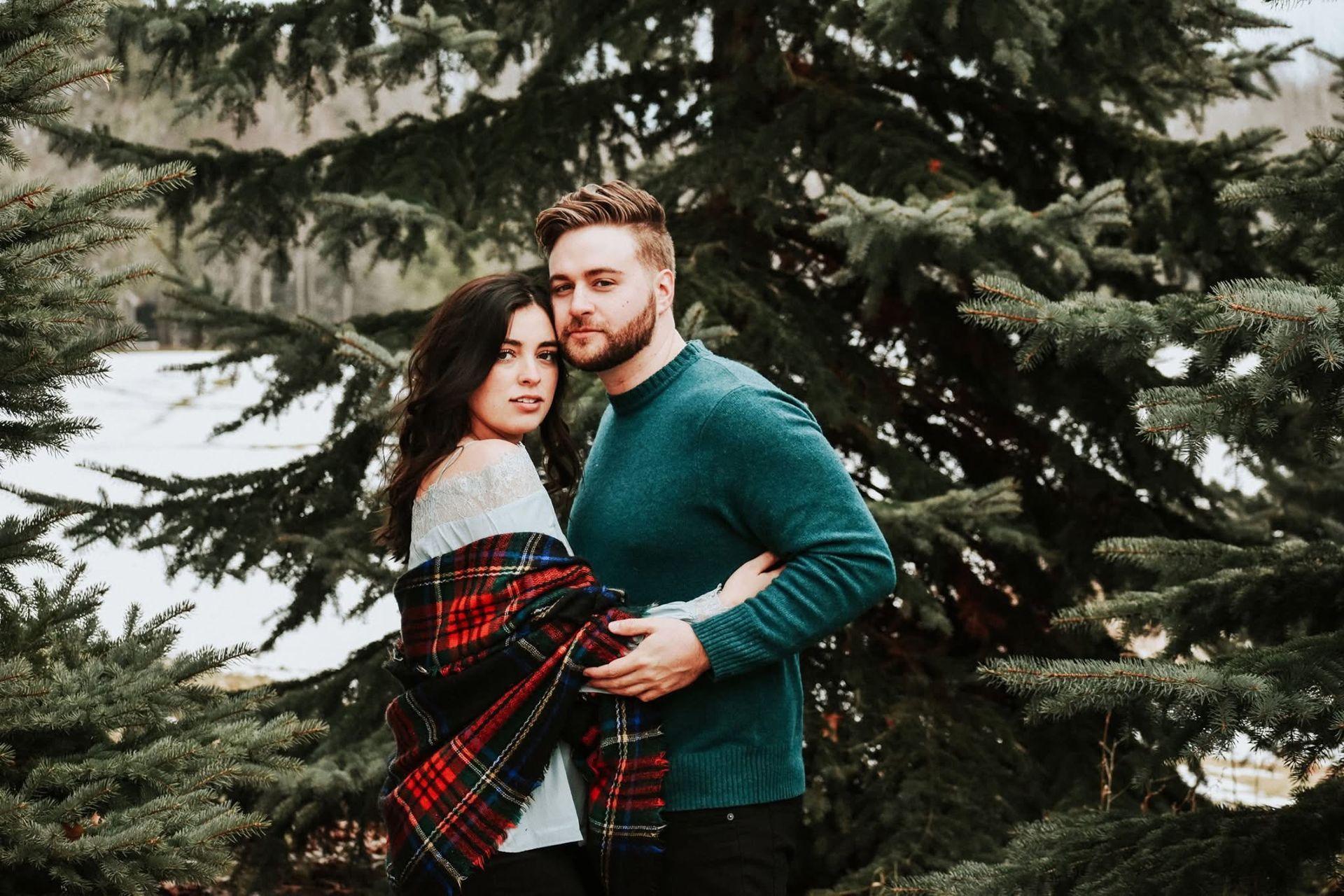 A man and a woman are standing next to each other in front of a christmas tree.