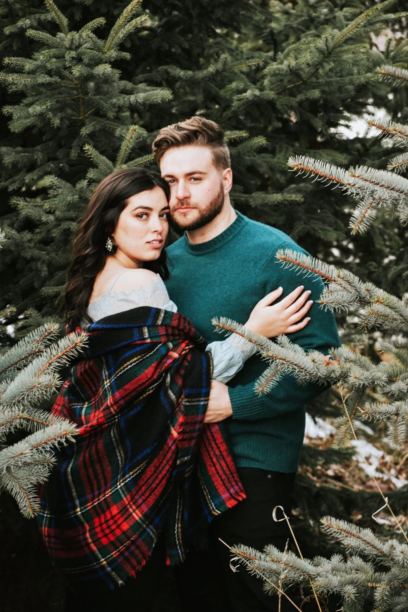 A man and a woman are standing next to each other in front of a christmas tree.