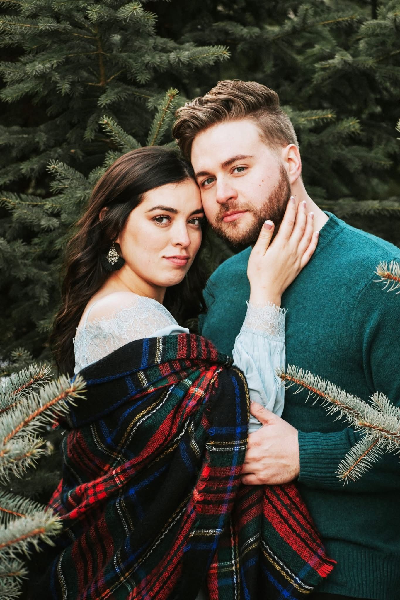 A man and a woman are posing for a picture in front of a christmas tree.