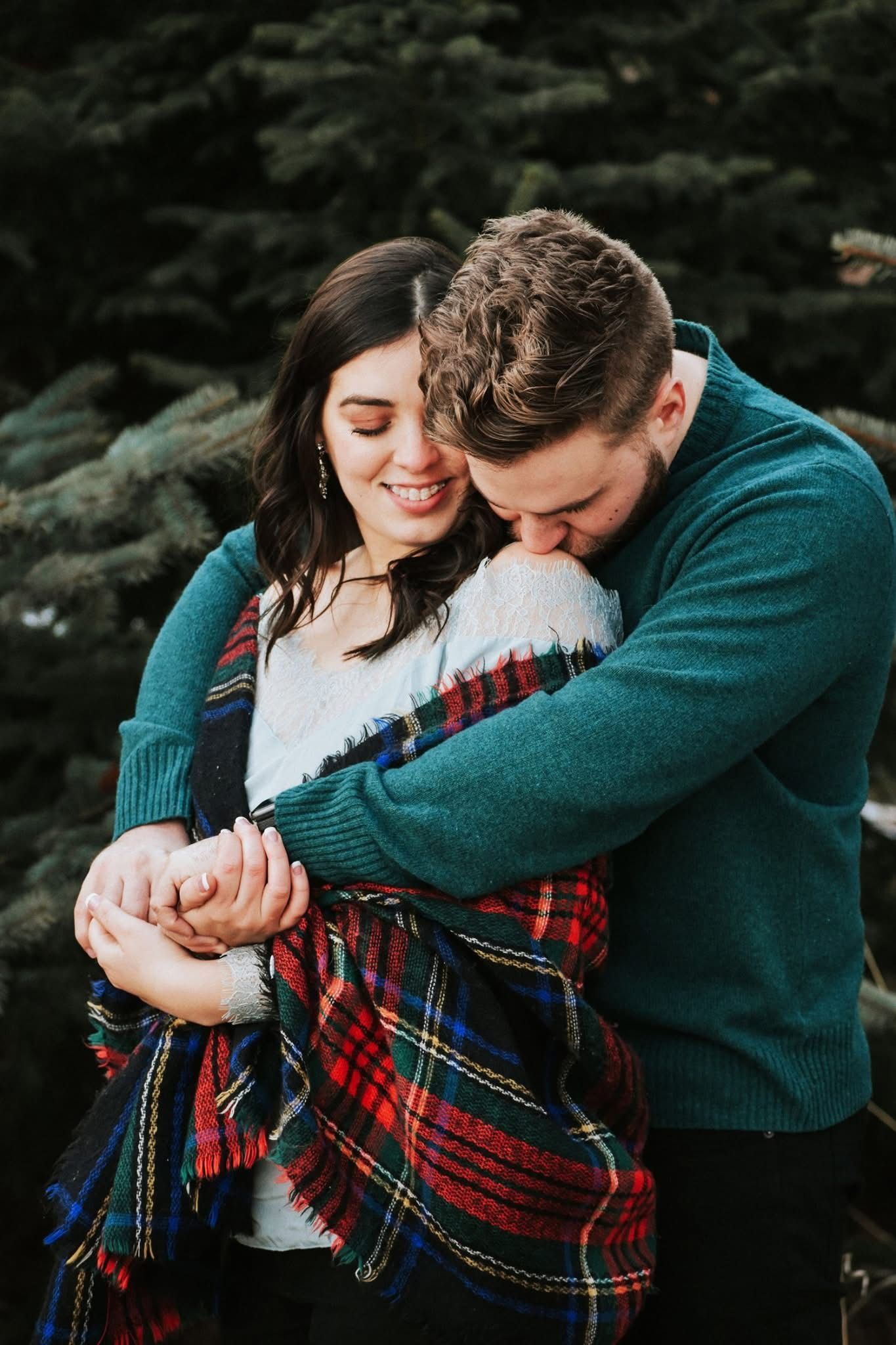 A man and a woman are hugging each other in front of a christmas tree.