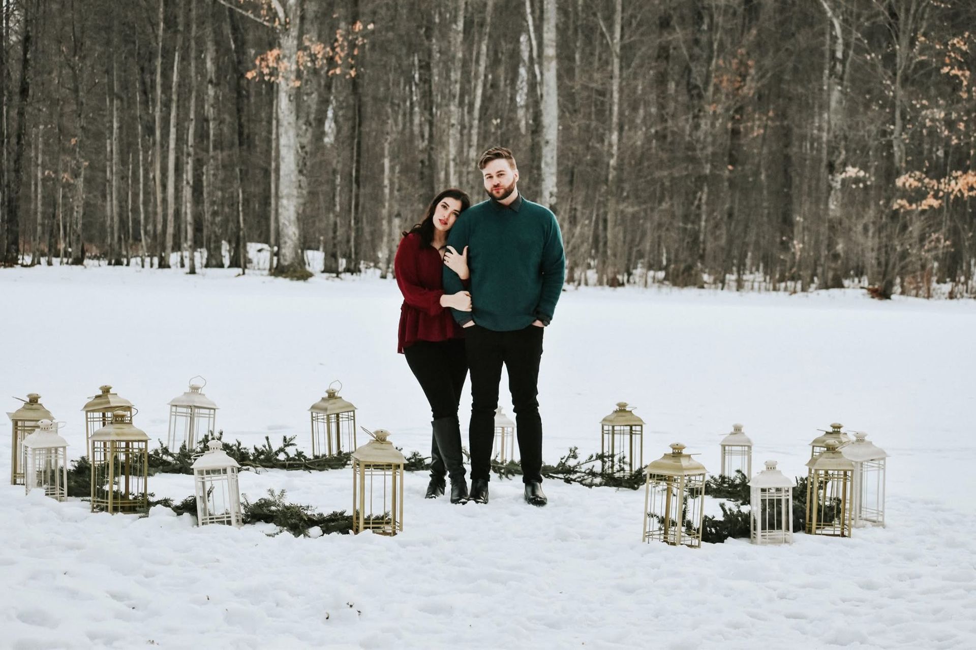 A man and a woman are standing in the snow surrounded by lanterns.