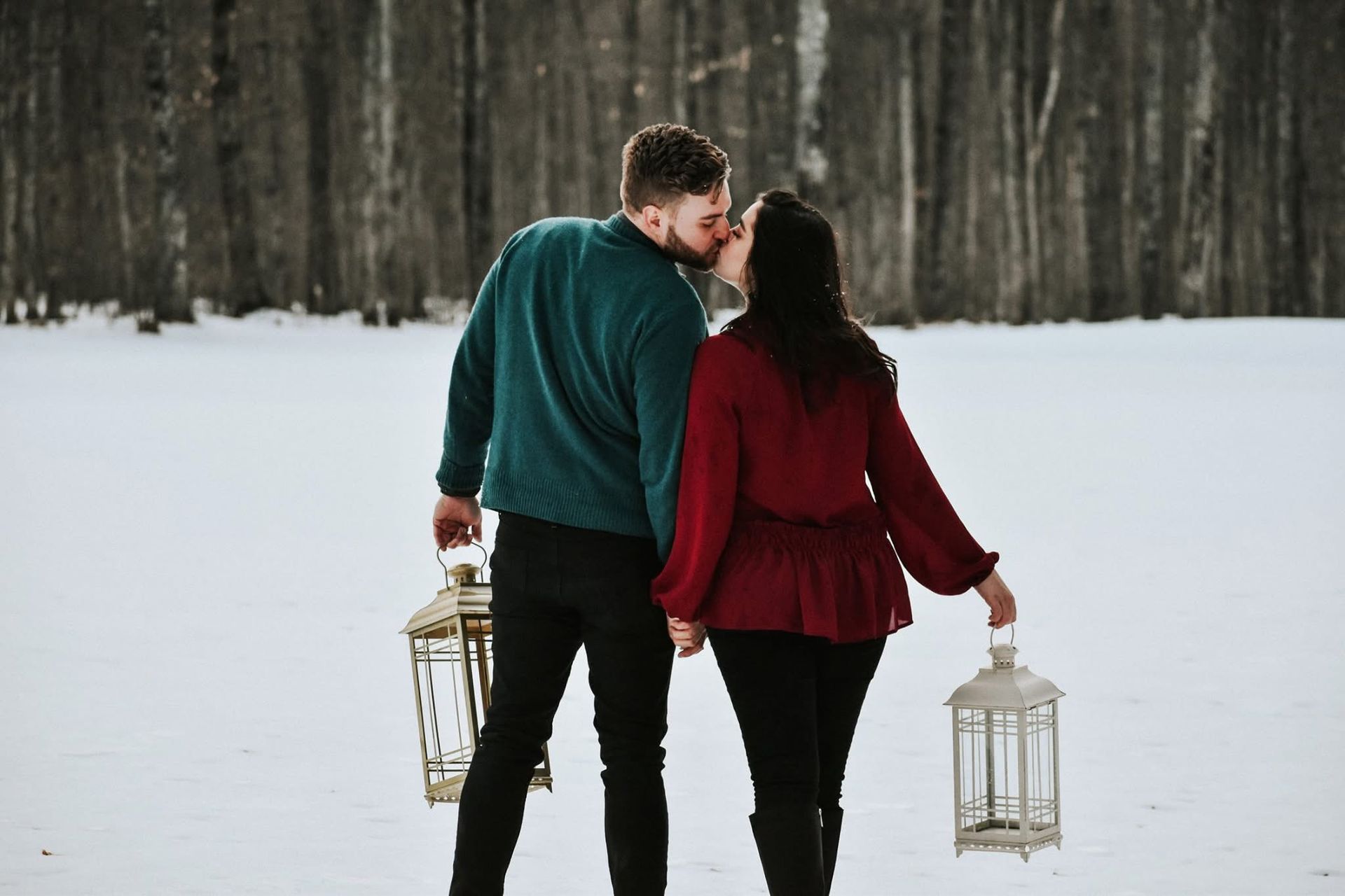 A man and a woman are kissing in the snow while holding lanterns.