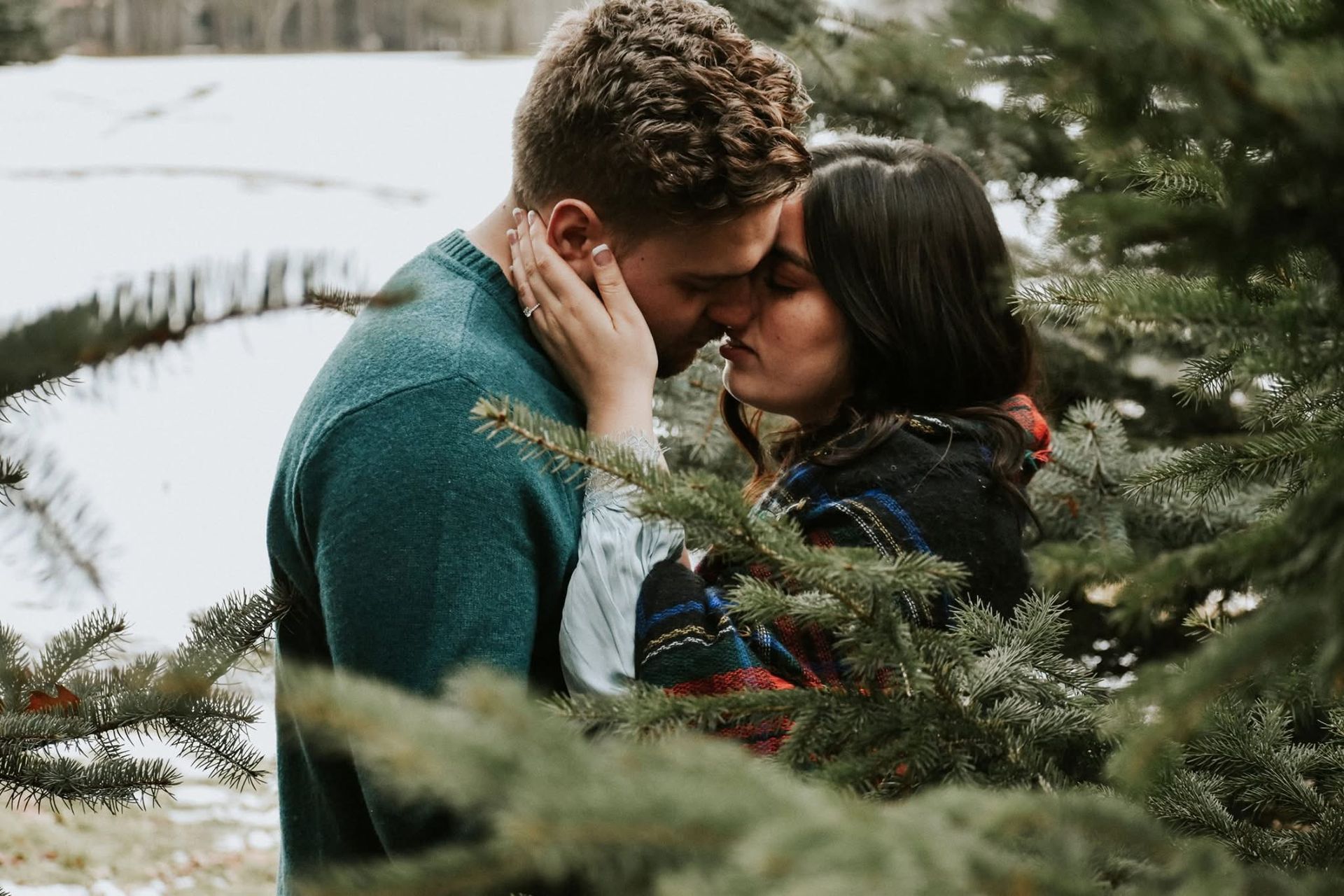A man and a woman are kissing in front of a christmas tree.