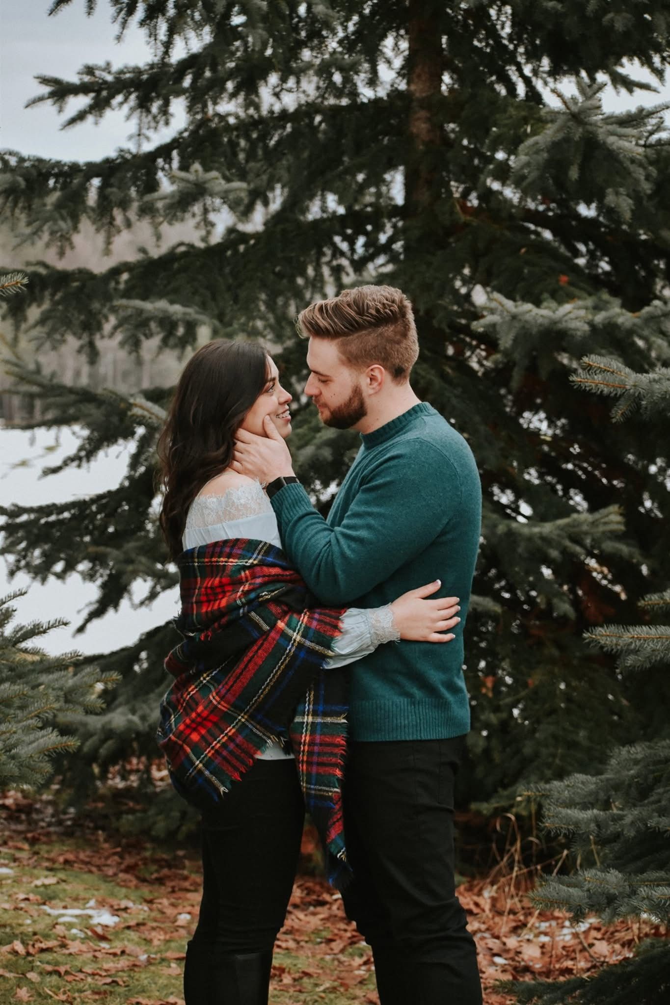 A man and a woman are hugging each other in front of trees.
