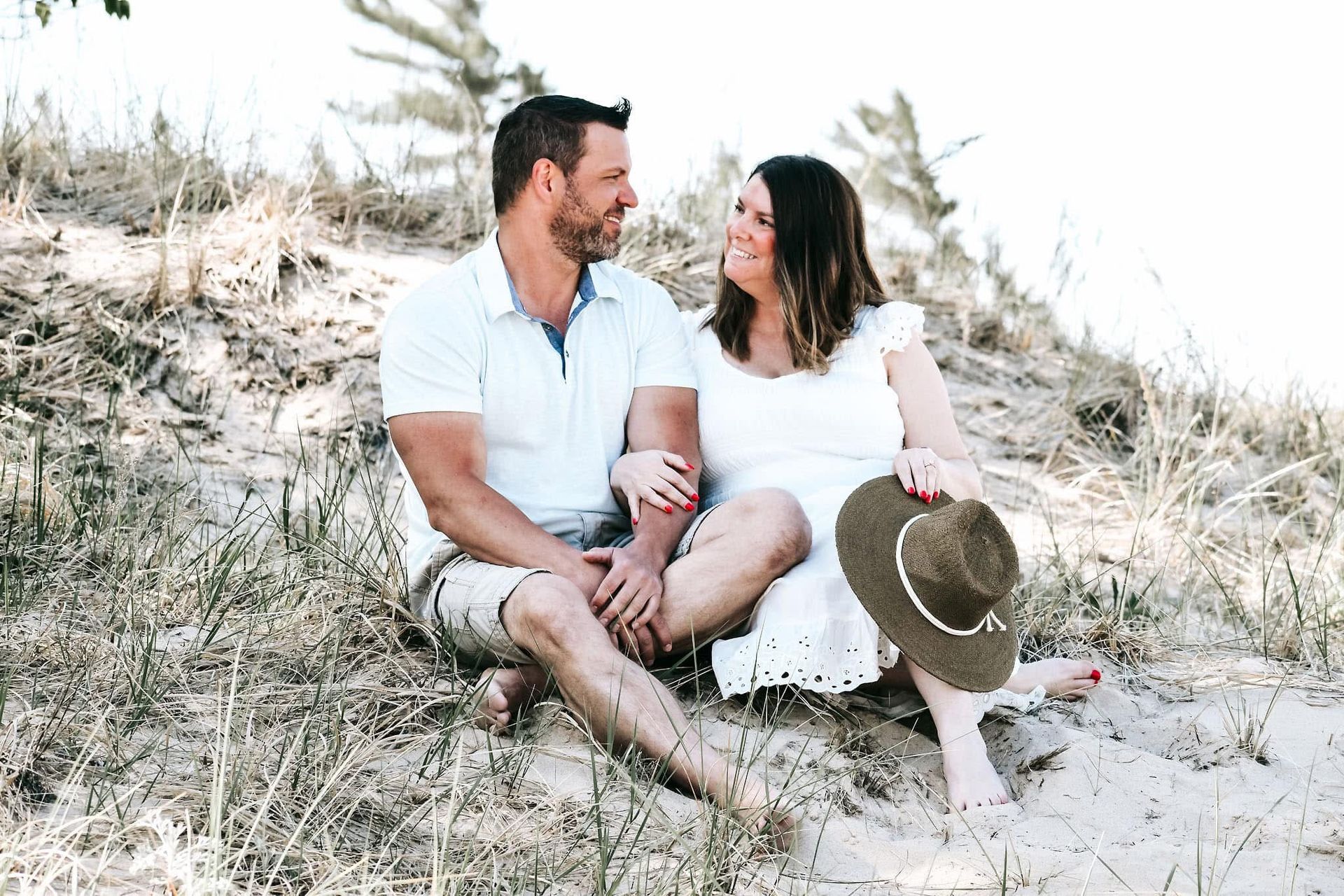 A man and a woman are sitting on top of a sand dune.