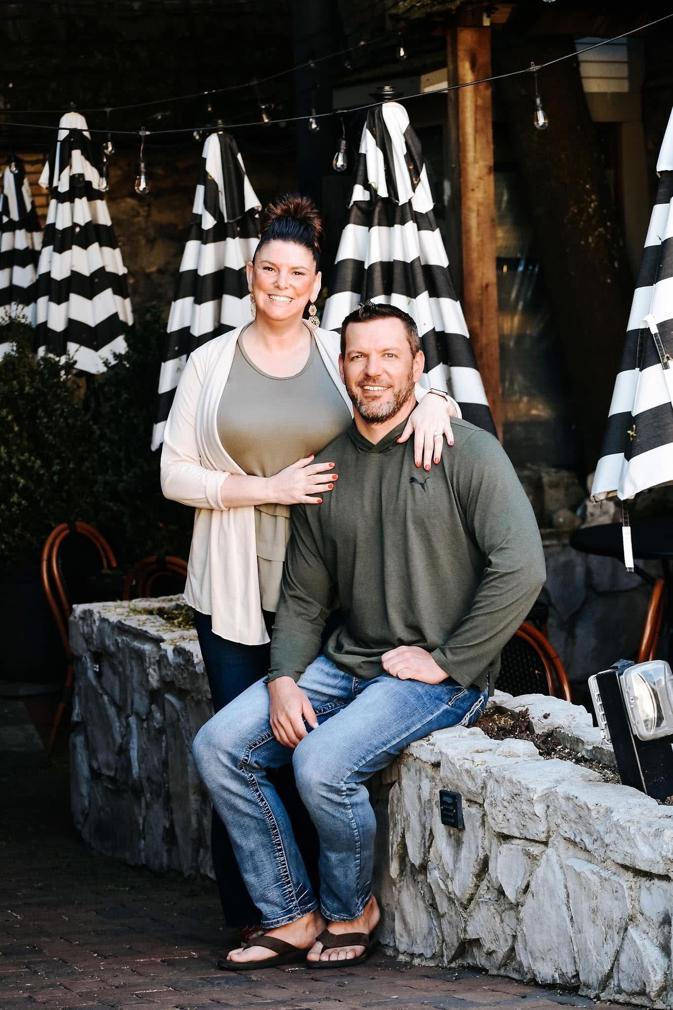 A man and a woman are posing for a picture while sitting on a stone wall.
