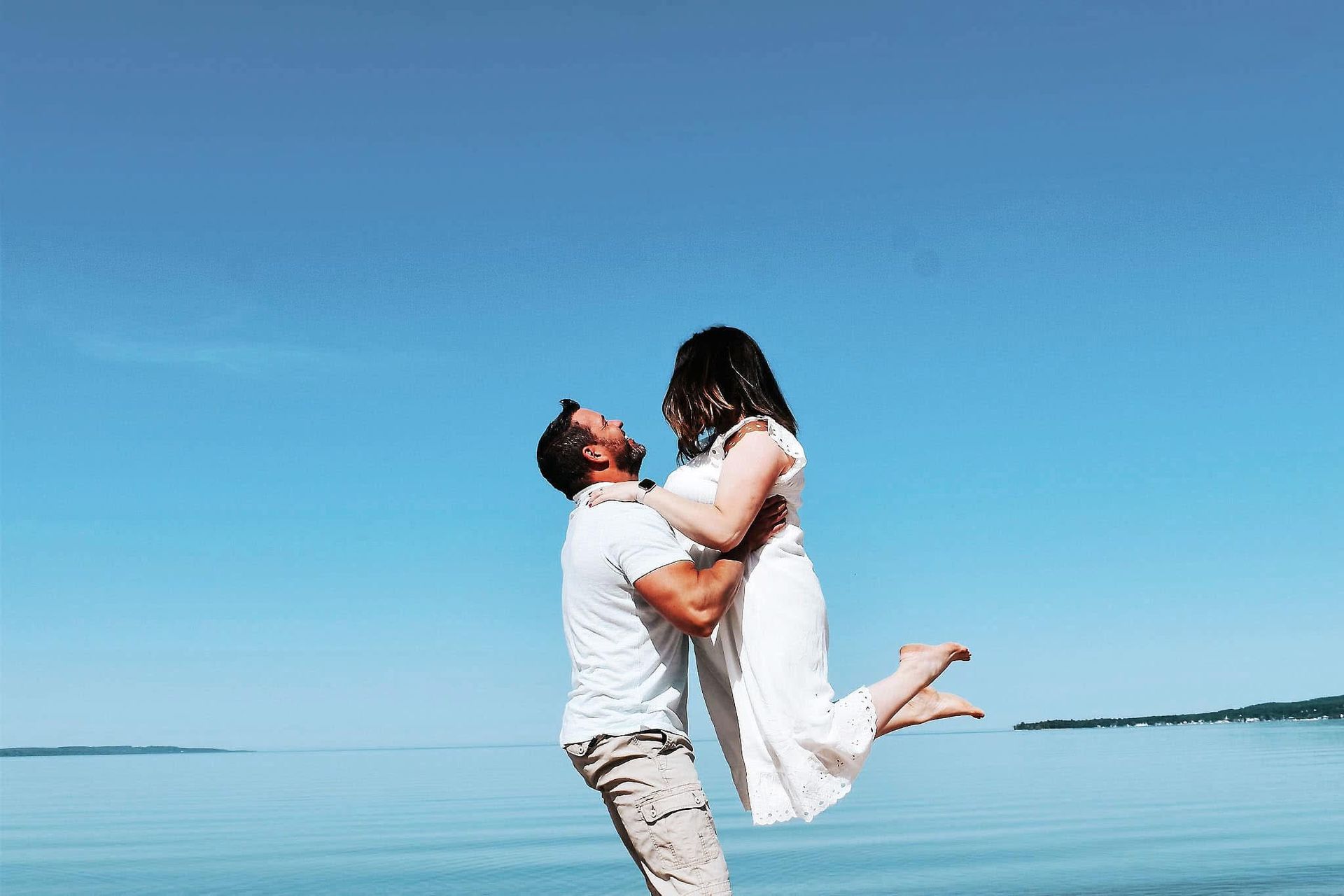 A man is holding a woman in his arms on the beach.