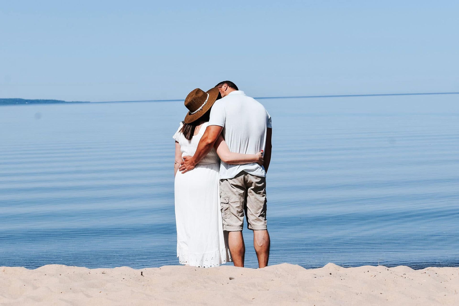 A man and a woman are standing on a beach looking at the ocean.