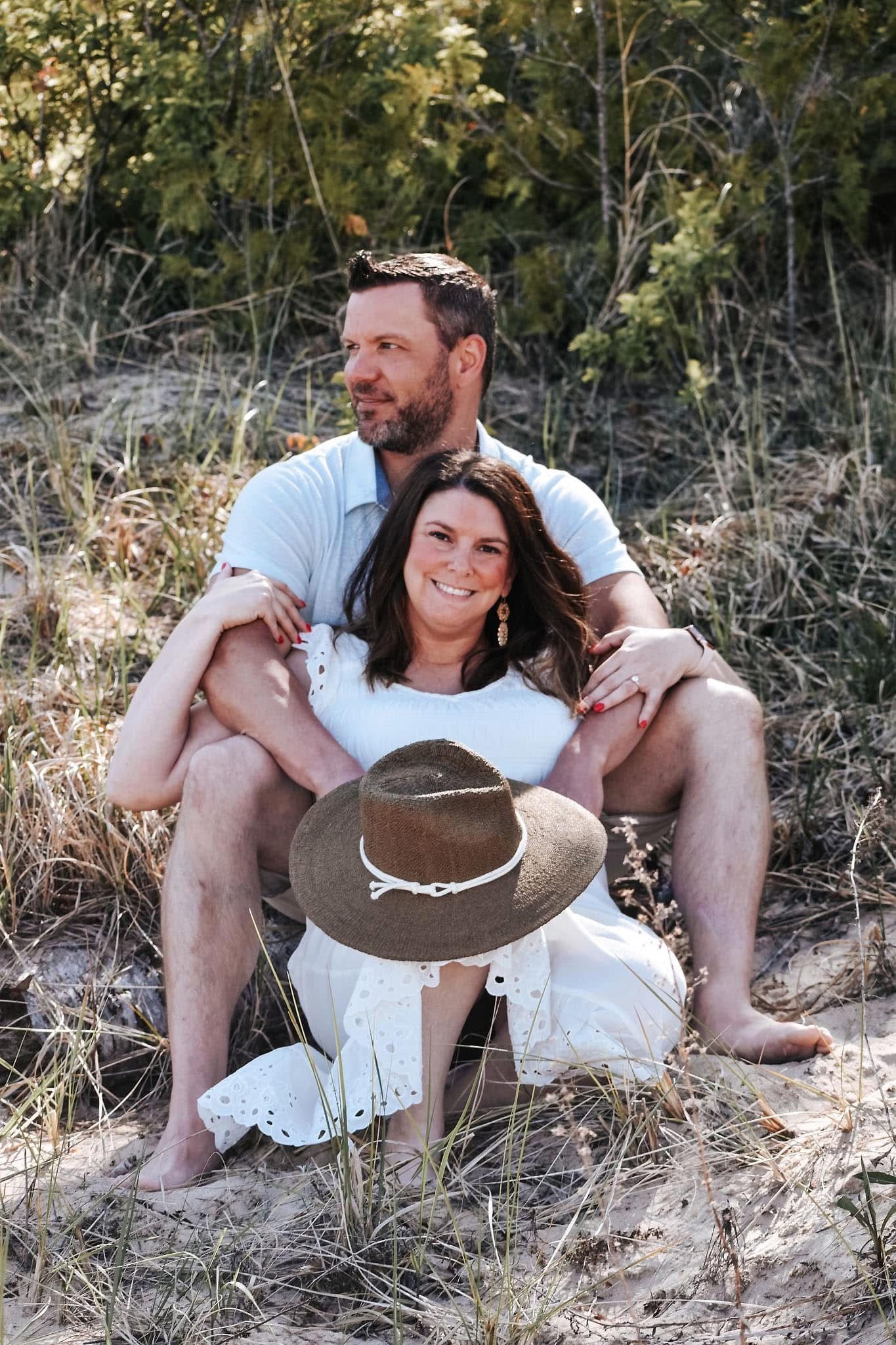 A man and a woman are sitting on top of a sand dune . the woman is wearing a hat.