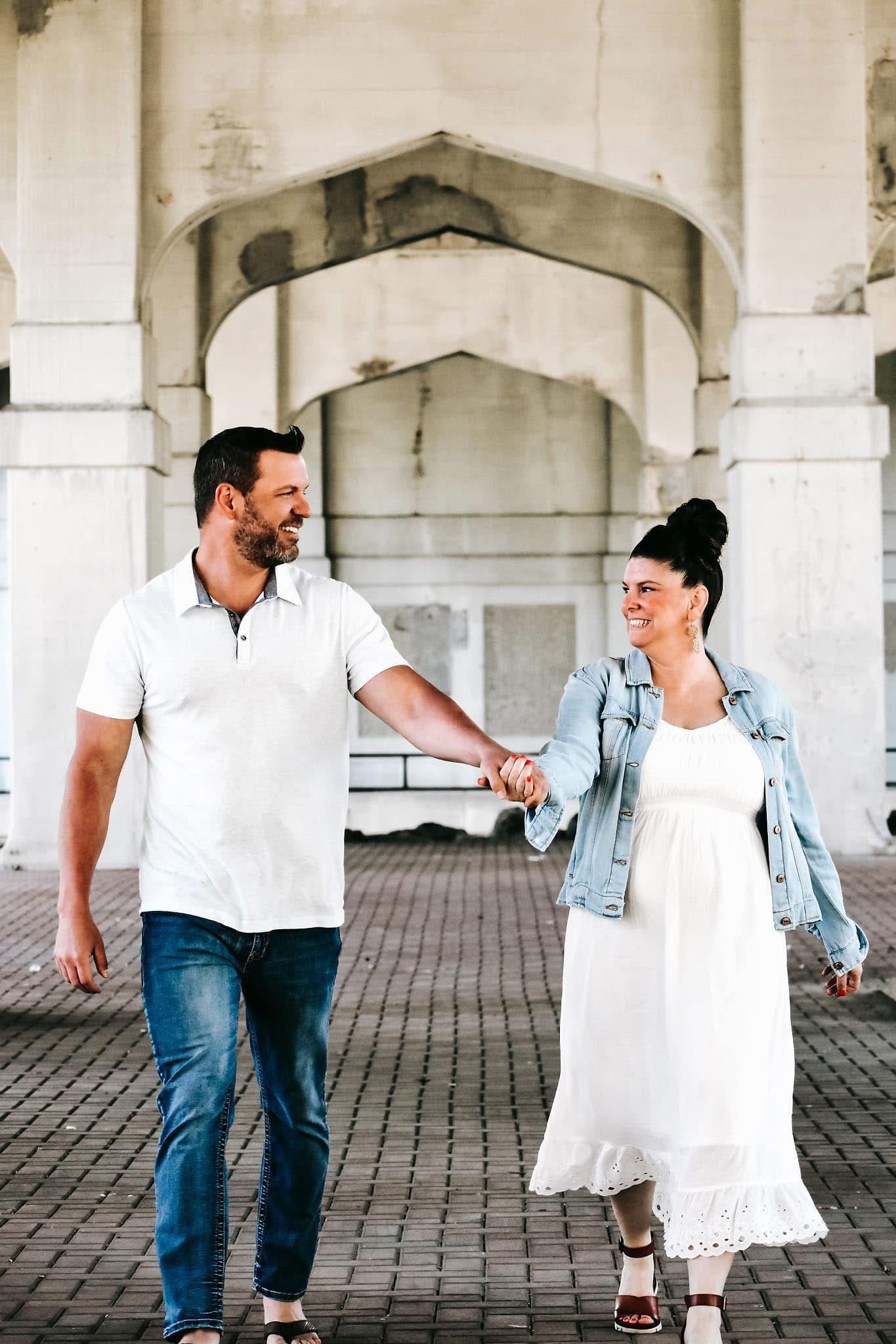 A man and a woman are holding hands while walking under a bridge.