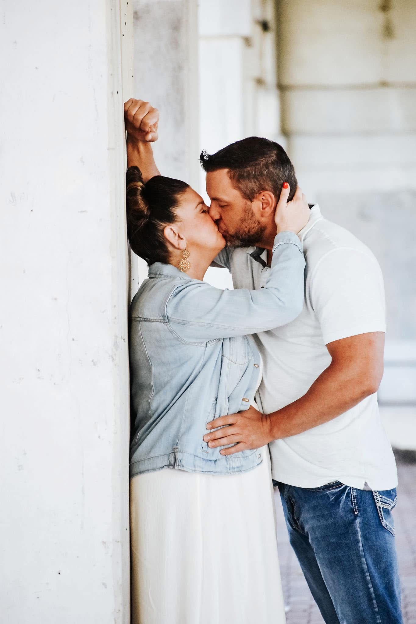 A man and a woman are kissing against a wall.