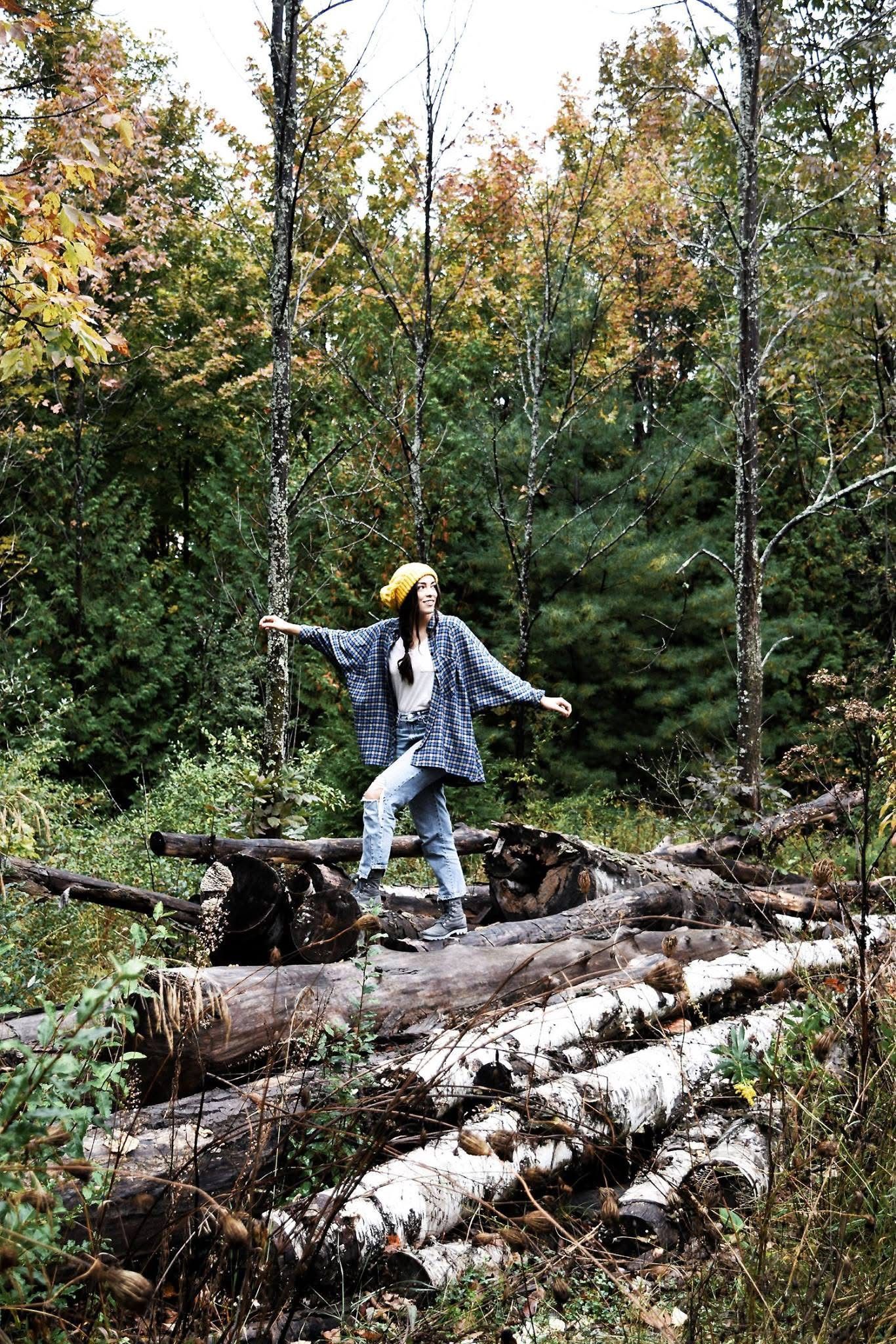 A woman is standing on a log in the middle of a forest.