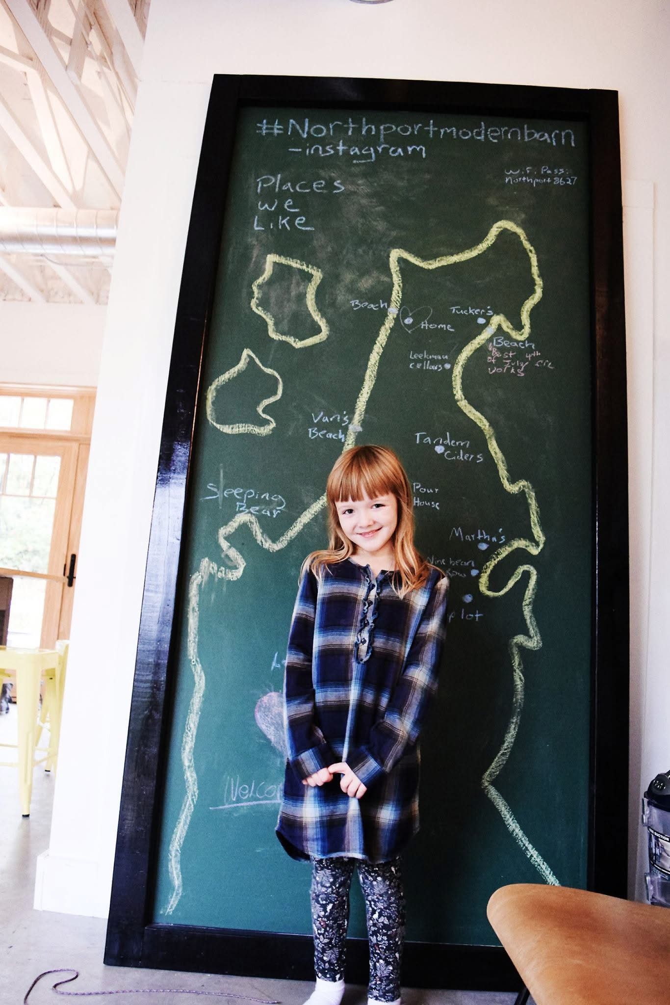 A girl stands in front of a large blackboard with a map drawn on it